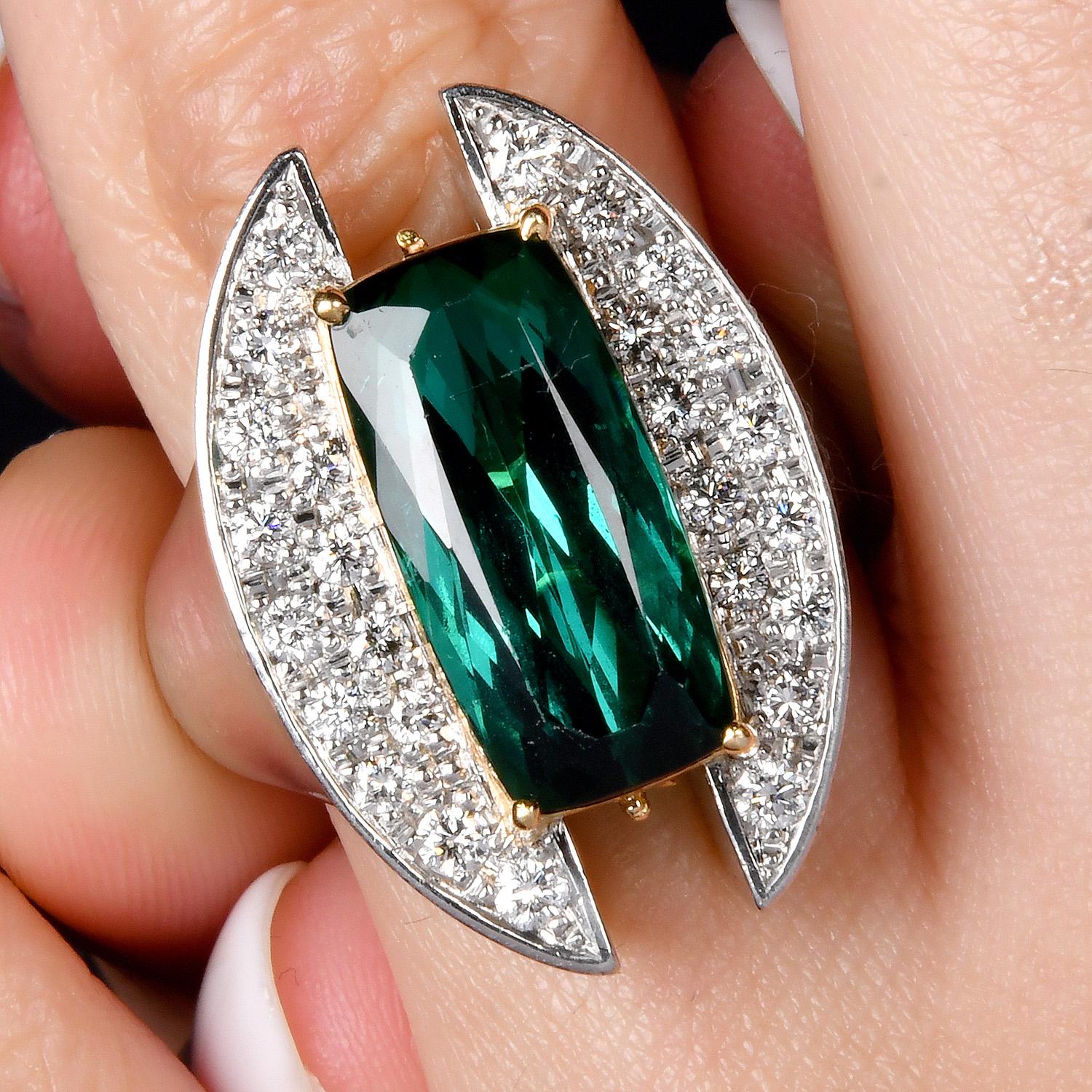 A bold and architectural masterpiece, this sculptural ring features a mesmerizing elongated green tourmaline, prong-set in rich 18K yellow gold. A wide platinum band, pavé-set with natural round brilliant diamonds frame the gemstone. A hidden