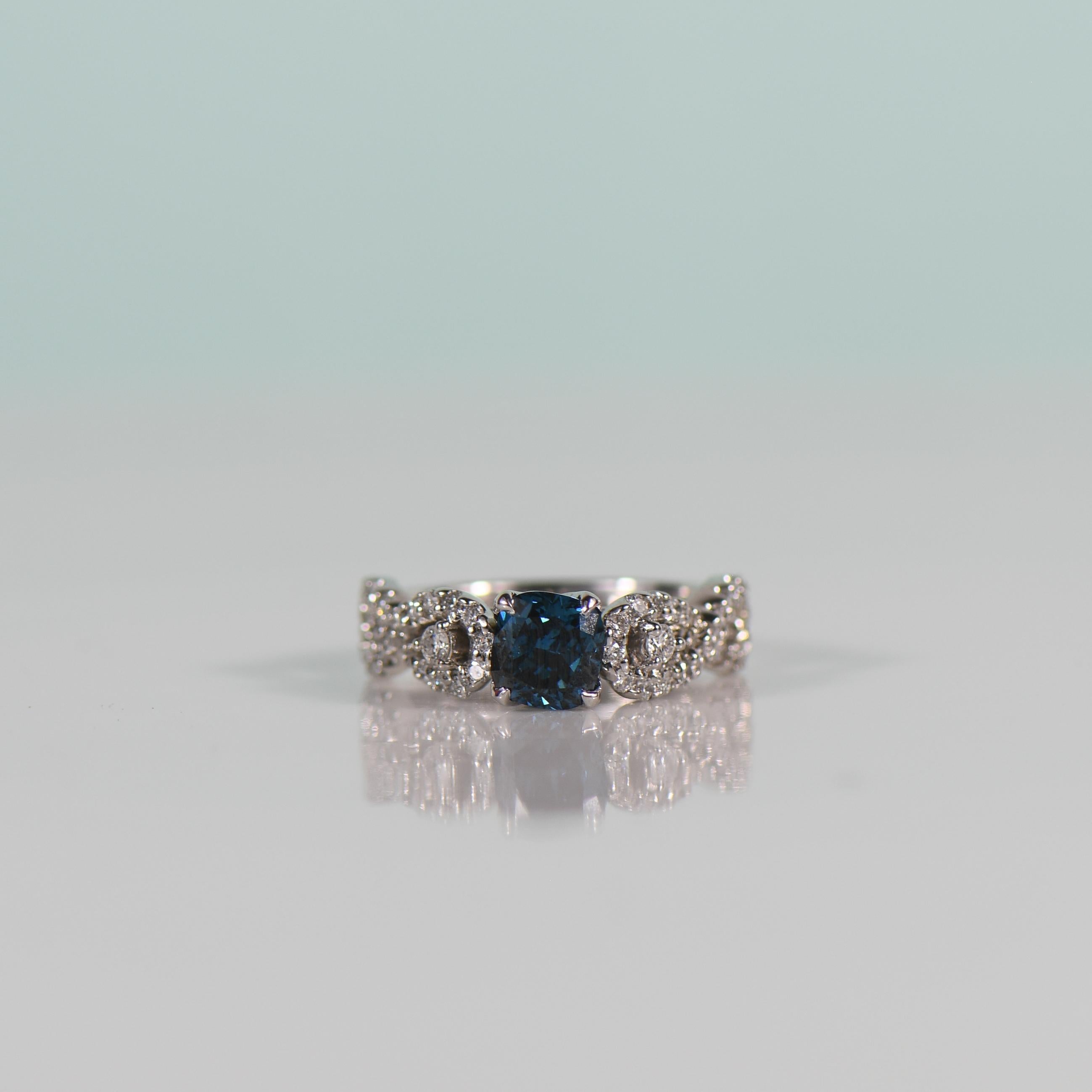 Elevate your love story with this mesmerizing Electric Blue 1.04 carat cushion cut diamond engagement ring, adorned within a stunning diamond infinity band. The vibrant hue of the diamond is reminiscent of deep ocean depths, capturing attention with