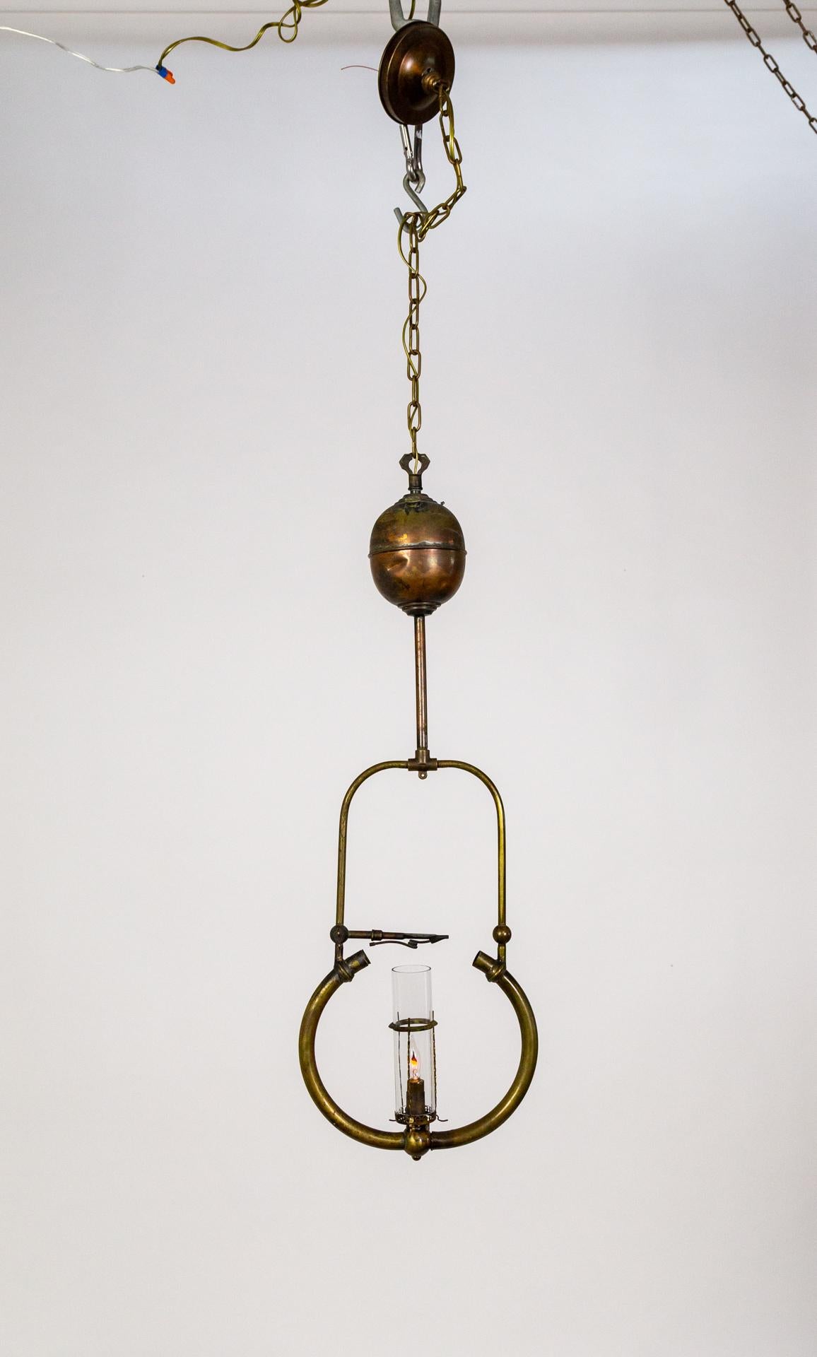 An antique, hanging pressure-style gas lamp.  Comprised of a brass harp structure topped with a stem and globular font, hanging by a chain.  It has a narrow cylindrical glass shade and candelabra socket.  Circa 1912. Newly wired.  12