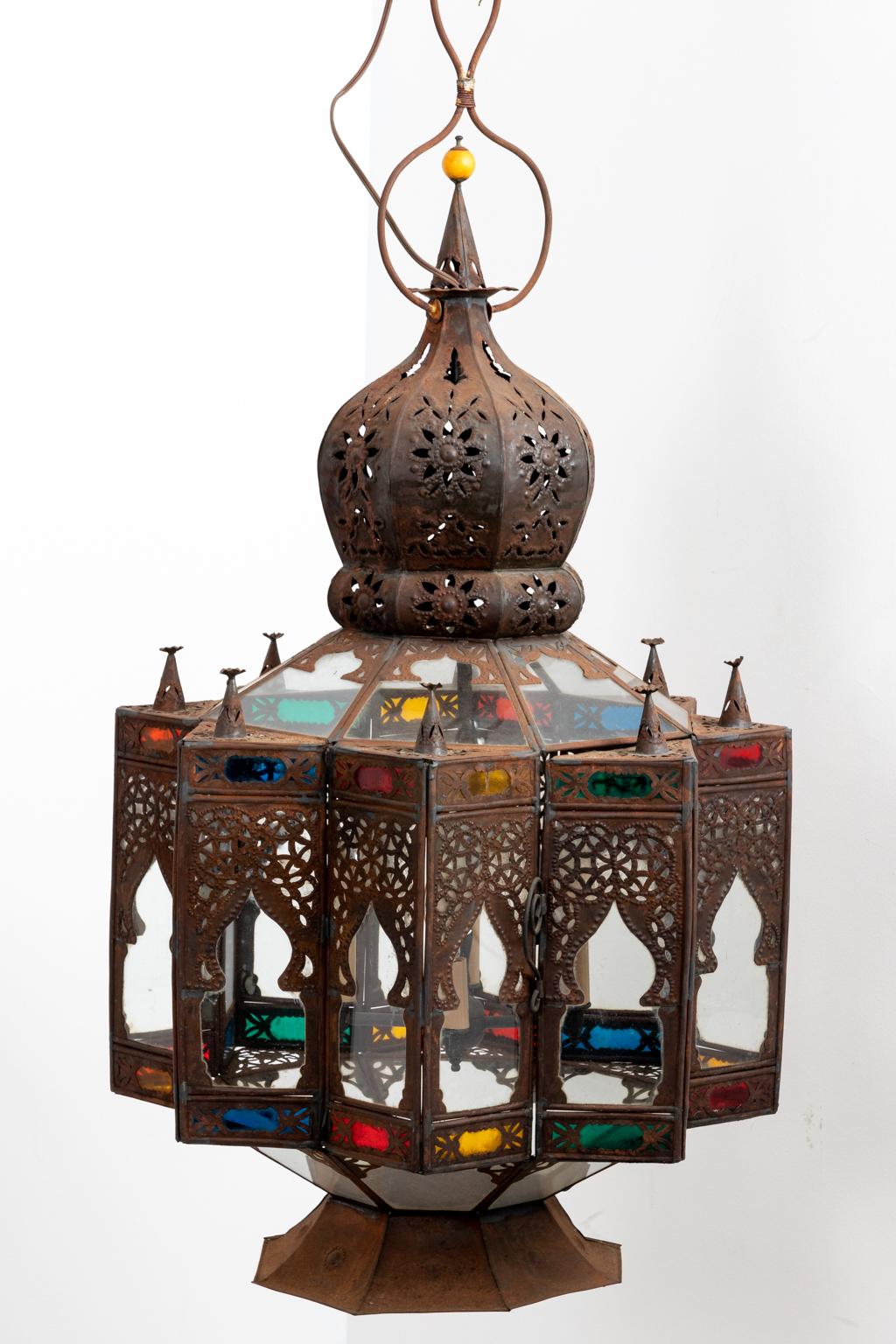 Circa 20th century Moroccan style electrified tin lantern with clear and color stained glass. The lantern also features decorative Arabesque panels with geometric tracery and pointed arches. Made in Morocco. Please note of wear consistent with age