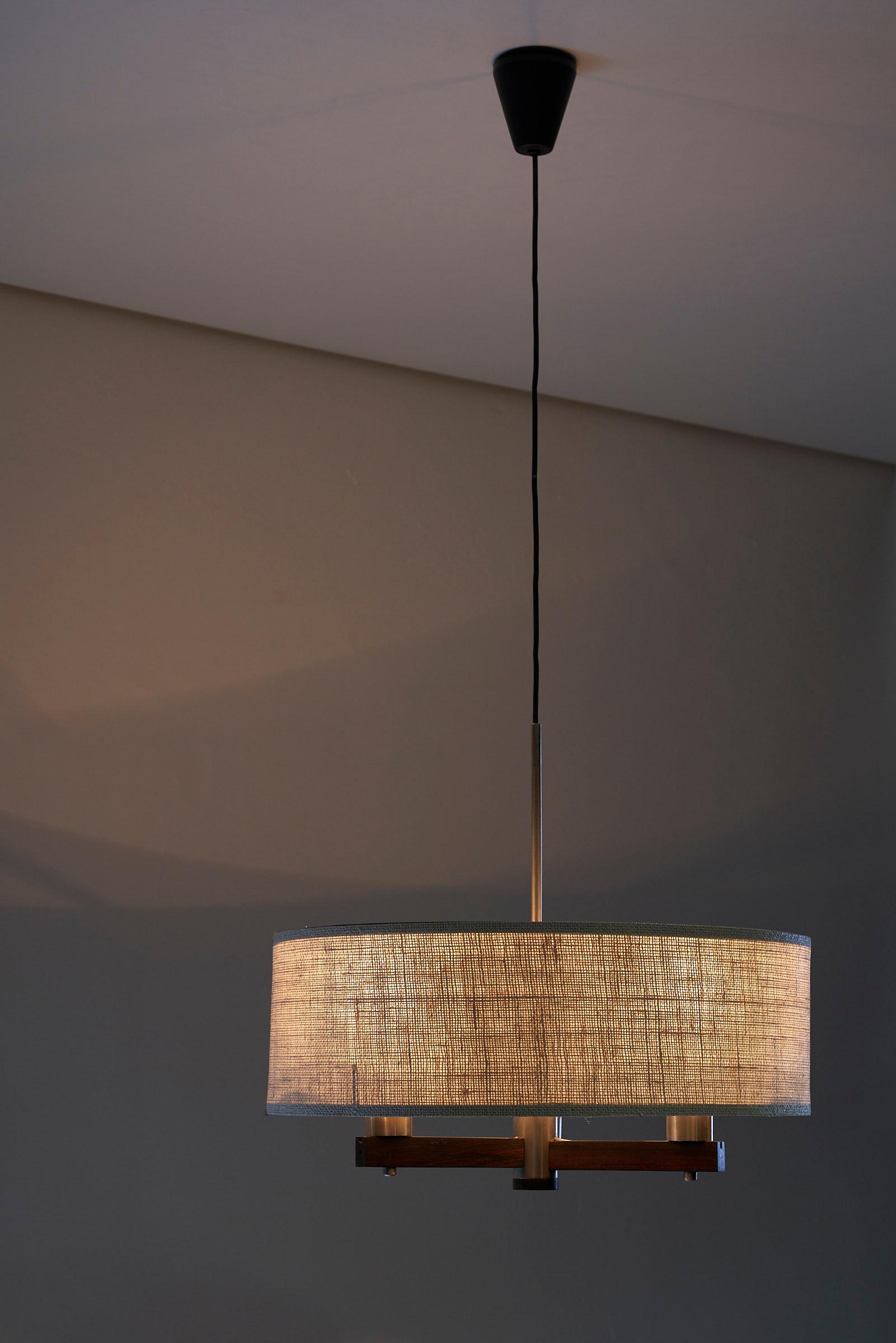 Introducing a captivating chandelier by Atelje Lyktan, a masterpiece that effortlessly combines elegance and functionality. This exquisite chandelier features wooden arms, a plexi diffuser surrounding the lightpoint, and a fabric shade enveloping