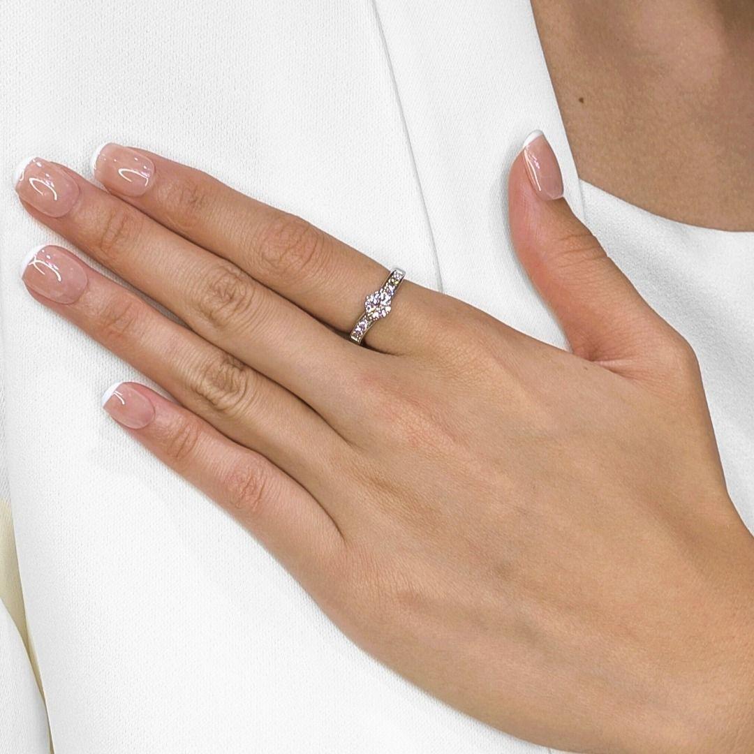 Este exquisito anillo de oro blanco de 18 quilates exhibe una belleza atemporal con un deslumbrante diamante brillante redondo de 0,62 quilates como pieza central, que irradia un fuego y un brillo excepcionales. Los hombros están elegantemente