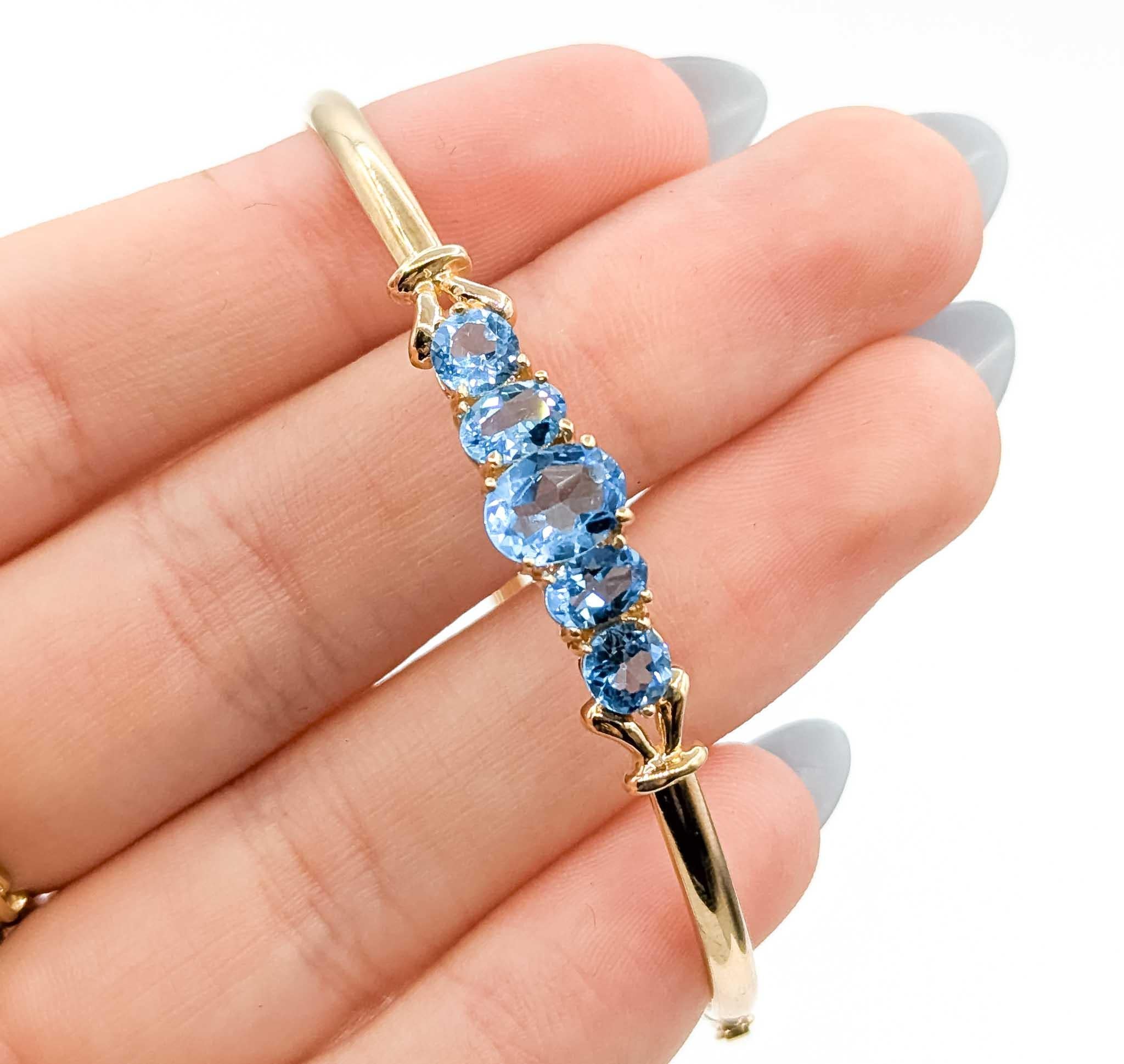 Questo raffinato bracciale è realizzato in oro giallo 10k e progettato in stile bangle flessibile per una vestibilità sicura e confortevole. Al centro, cinque gemme di topazio blu di taglio ovale per un totale di circa 3,80 carati sono incastonate,