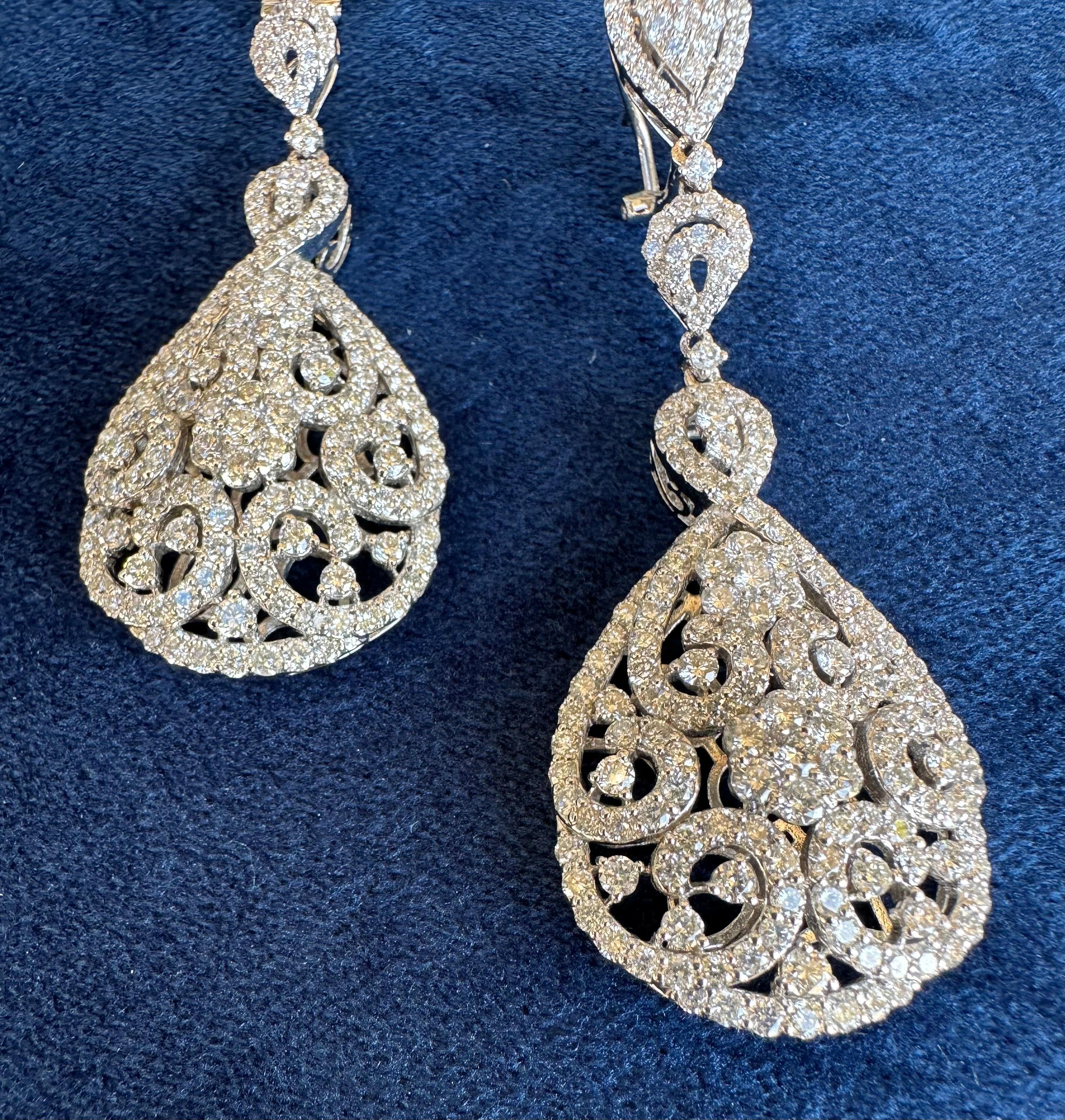 Very elegant, ladies 18 karat white gold pear shaped diamond cluster drop earrings feature a slightly domed center with an array of round brilliant diamonds in the center forming a flower which is surrounded by fancy swirling motifs cascading