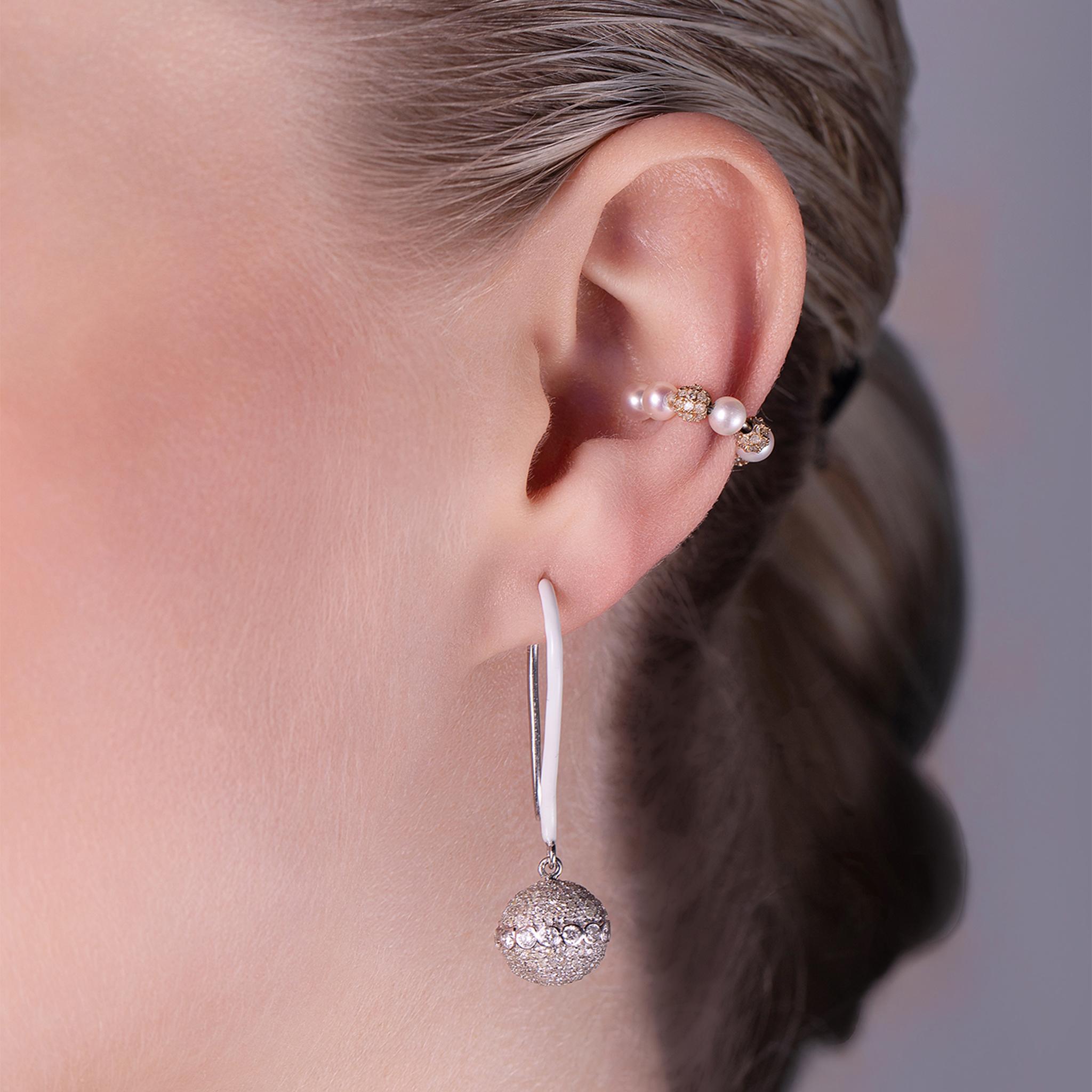 These exquisite 18-karat white gold earrings seamlessly blend sophistication and modern elegance. Partially adorned with crisp white enamel, they feature dazzling diamond orb charms meticulously crafted to reflect the flawless silhouette of an orb.