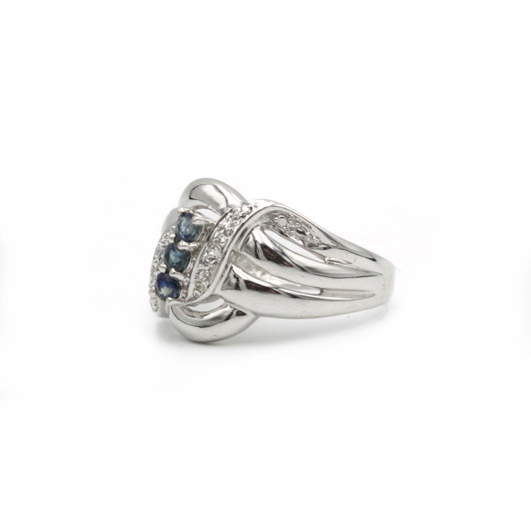 Questo sofisticato anello fonde un design fluido con vibranti accenti di gemme, creando un'opera d'arte da indossare. Realizzato in oro bianco lucido 18 carati, la fascia si divide in tre graziosi nastri che si intrecciano, evocando movimento ed