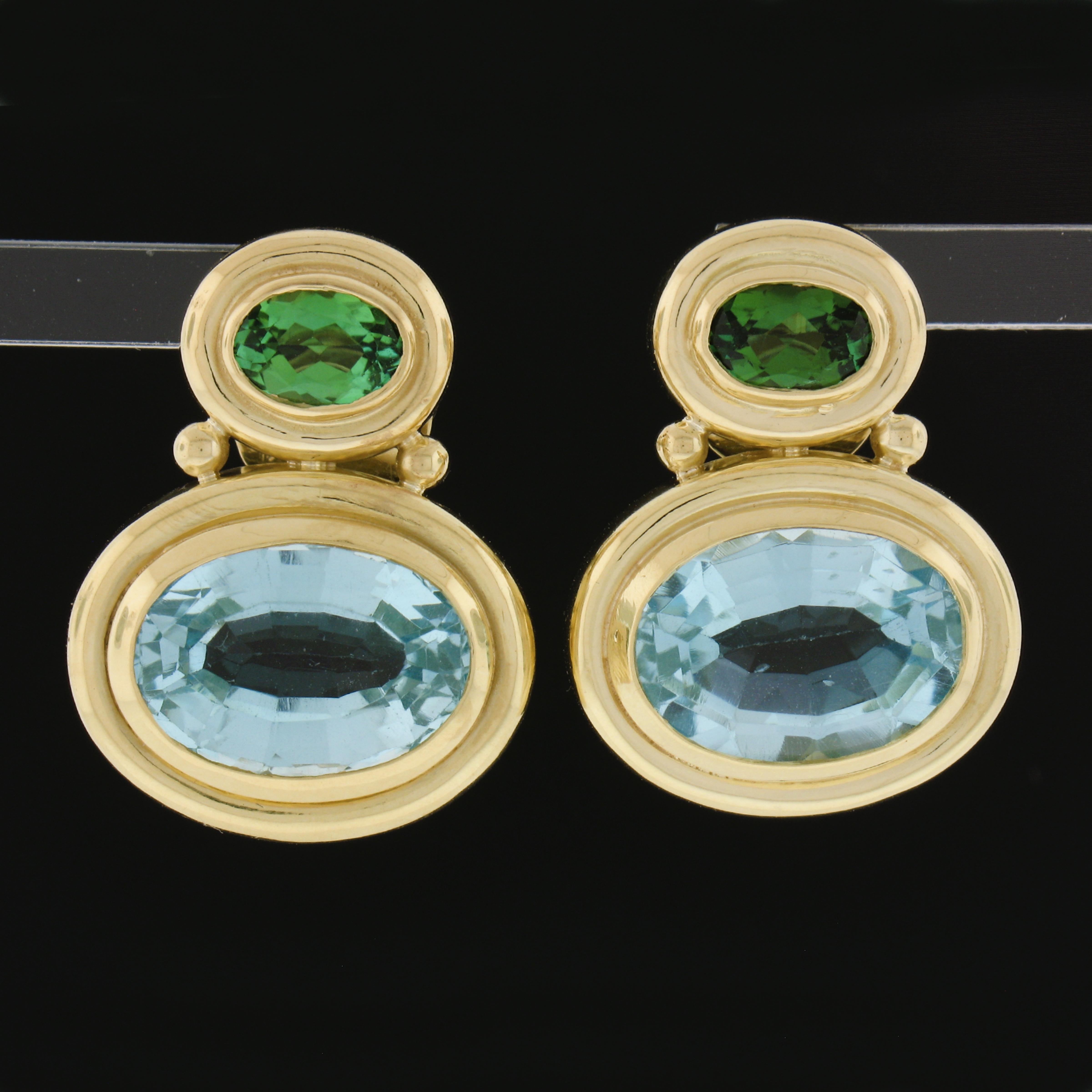 These beautiful elegant drop earrings are crafted from solid 18k yellow gold. They feature oval Blue topaz and oval green tourmaline stones. The stones are neatly bezel set in a simple polished frames. The earrings secure with posts and safe