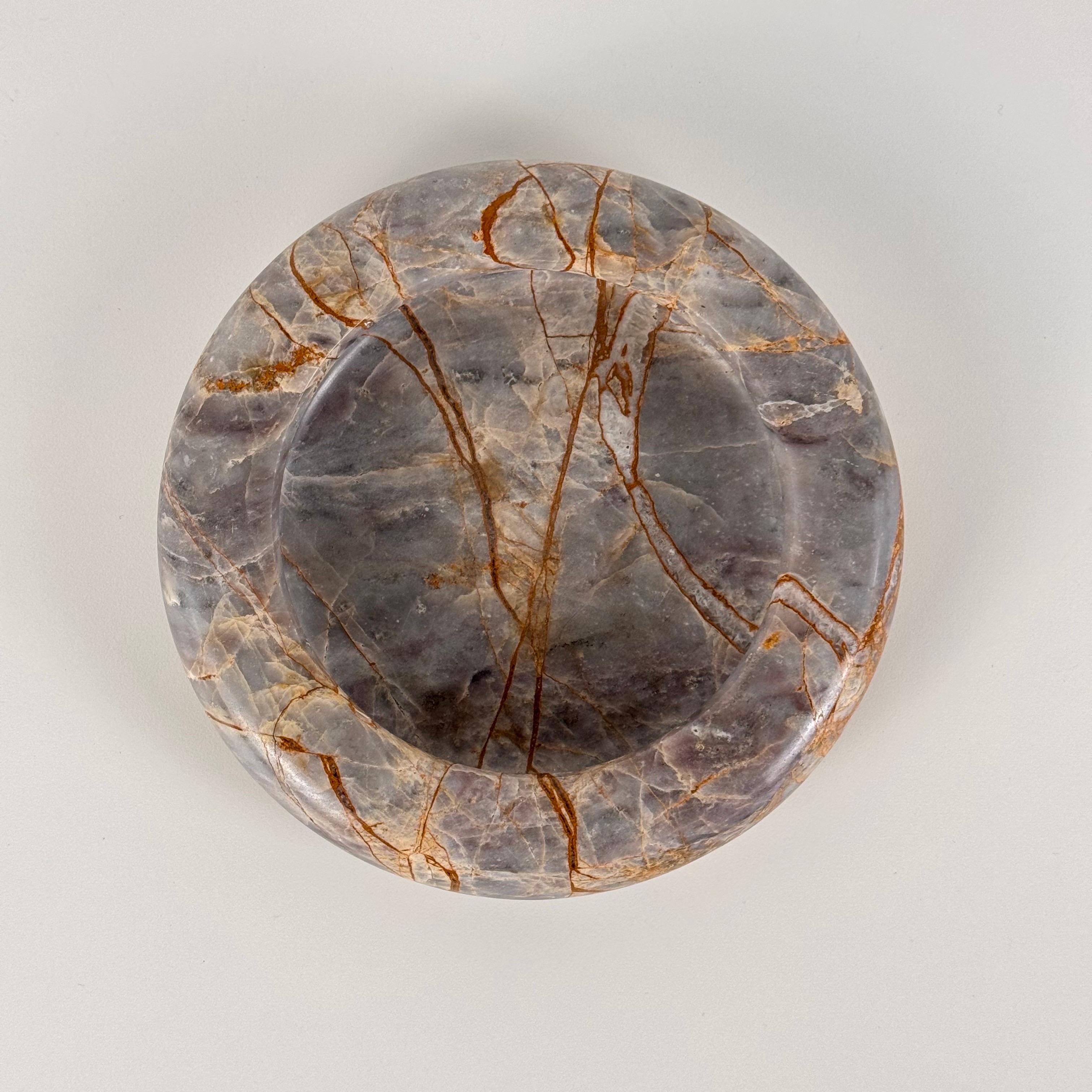 Este exquisito cenicero o bandejita, fabricado en mármol Breccia, es una pieza atemporal que capta la elegancia de los años setenta. El mármol presenta una asombrosa gama de tonos cálidos y terrosos -desde grises y blancos suaves hasta ricos matices