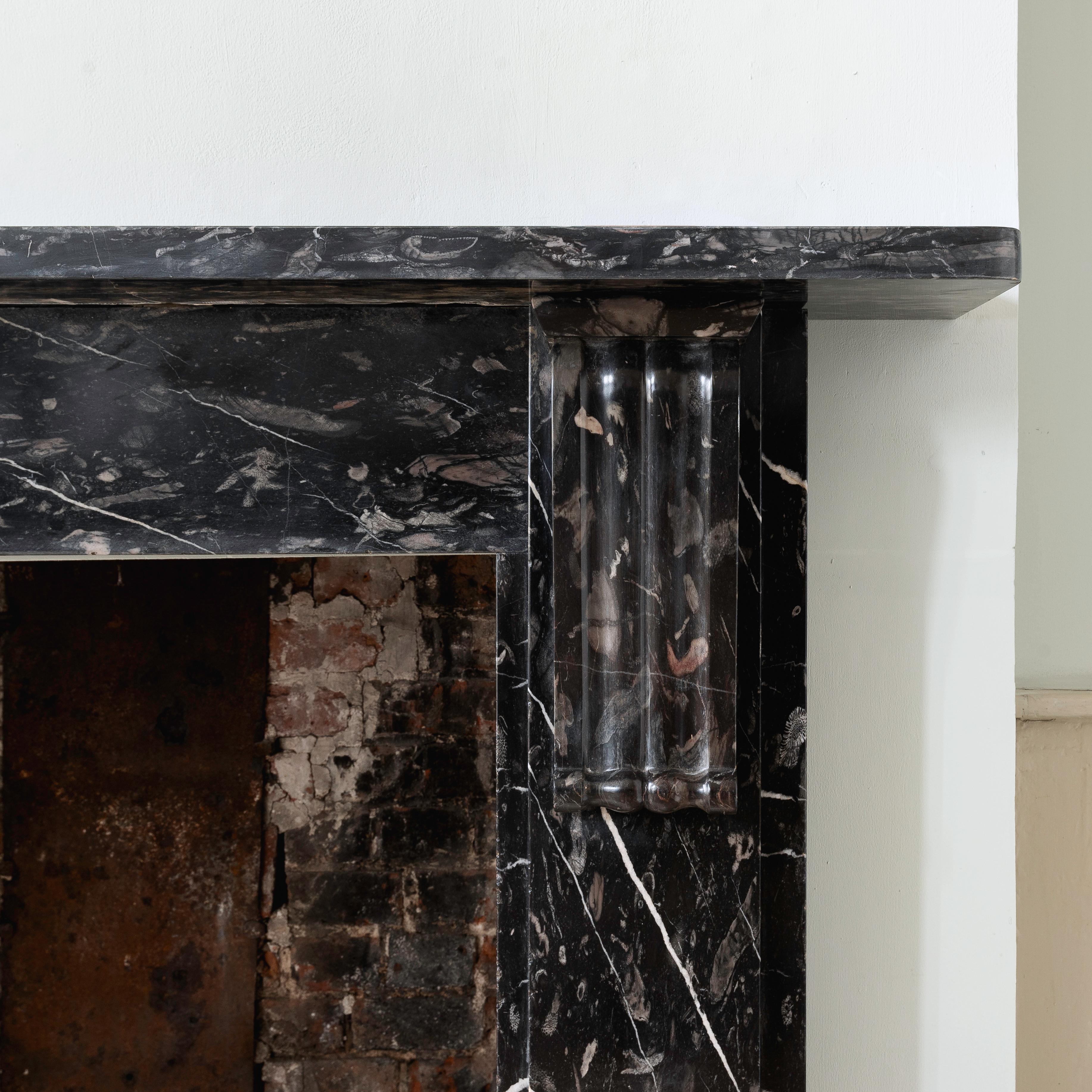 An elegant nineteenth century English fossiliferous chimneypiece in Plymouth Black limestone, of simple form with elongated corbels, carved in native limestone from the Radstock/Pomphlett mines of Plymouth, with an unusual abundance of
