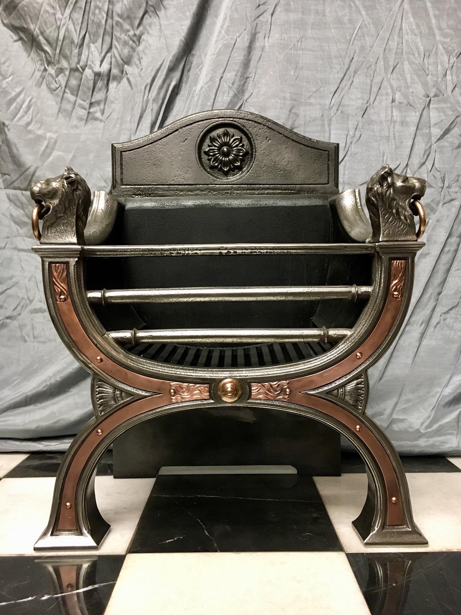 An elegant Regency style polished cast iron fire grate. A three bar arch front with bronze repousse inlays, mounted with a pair of grand lion masks holding bronze rings in their mouths, the shaped high back plate with a central stylized sunflower,