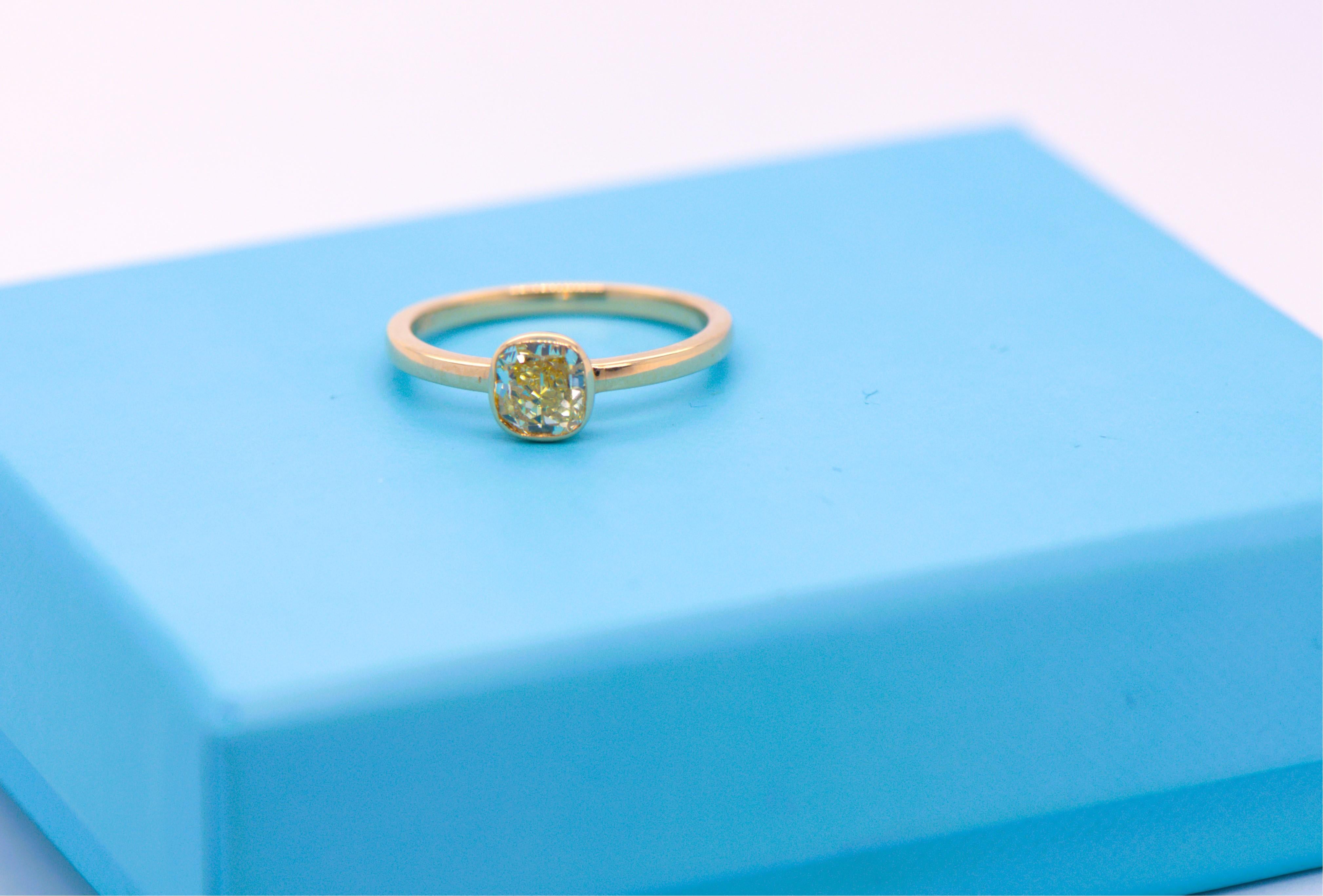 Discover the timeless elegance of this exquisite ring, featuring a natural earth-mined yellow cushion cut diamond weighing 1 carat. The stunning diamond is set in a sleek bezel solitaire, crafted from luxurious 18kt yellow gold. This ring is perfect