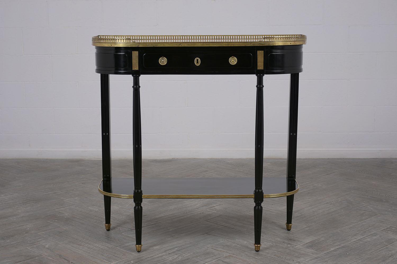 This elegant Louis XVI style demilune console table features an ebonized finish with a brass gallery that surrounds the ivory colored marble top. The single drawer has double brass pulls with working lock and key. The console has sturdy carved legs