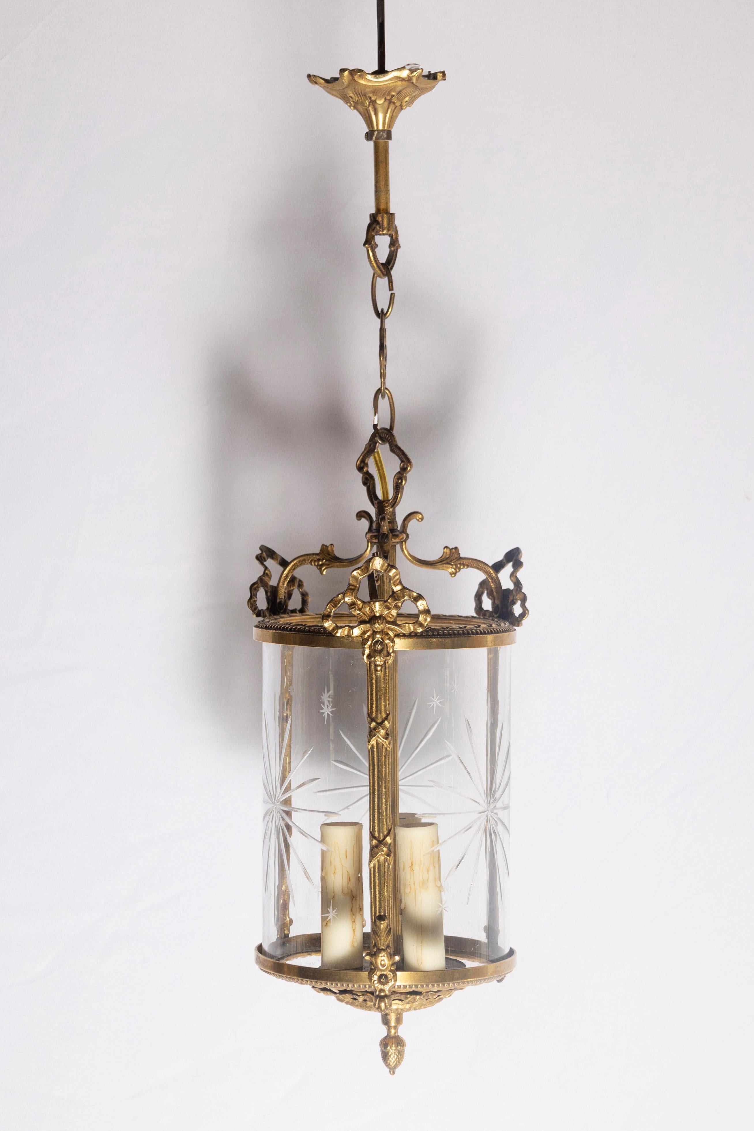 This exquisite early 20th-century French lantern exudes timeless elegance with its finely detailed gilt brass frame and intricate craftsmanship. The cylindrical form is enclosed by beveled glass panels, each adorned with delicate starburst etching,