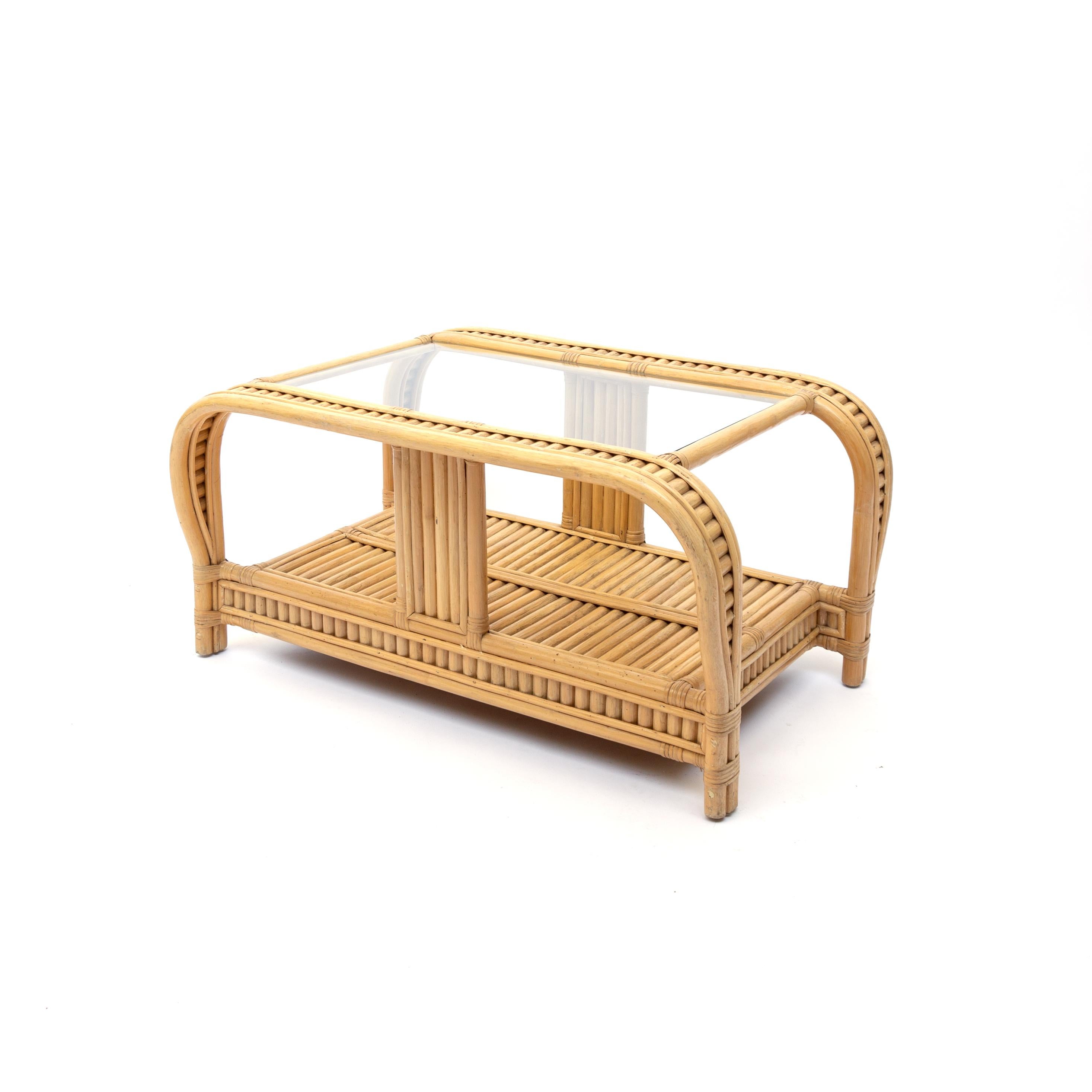 Made circa 1970s, this 3-pole rattan coffee table has an unusual bent rattan round sides carrying the glass top. The 3 rattan poles are stacked together in a double C-shape. The glass top rests on it, exuding an almost floating quality. 