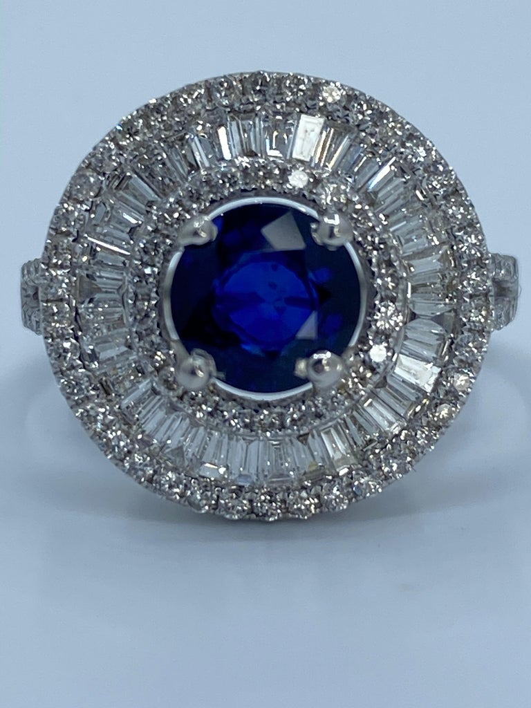 Timeless and elegant cocktail or engagement ring features a round cut vivid dark blue faceted sapphire, prong-set in the center. Surrounding the sapphire is a sparkling halo of invisibly set baguette diamonds creating a ballerina design. The