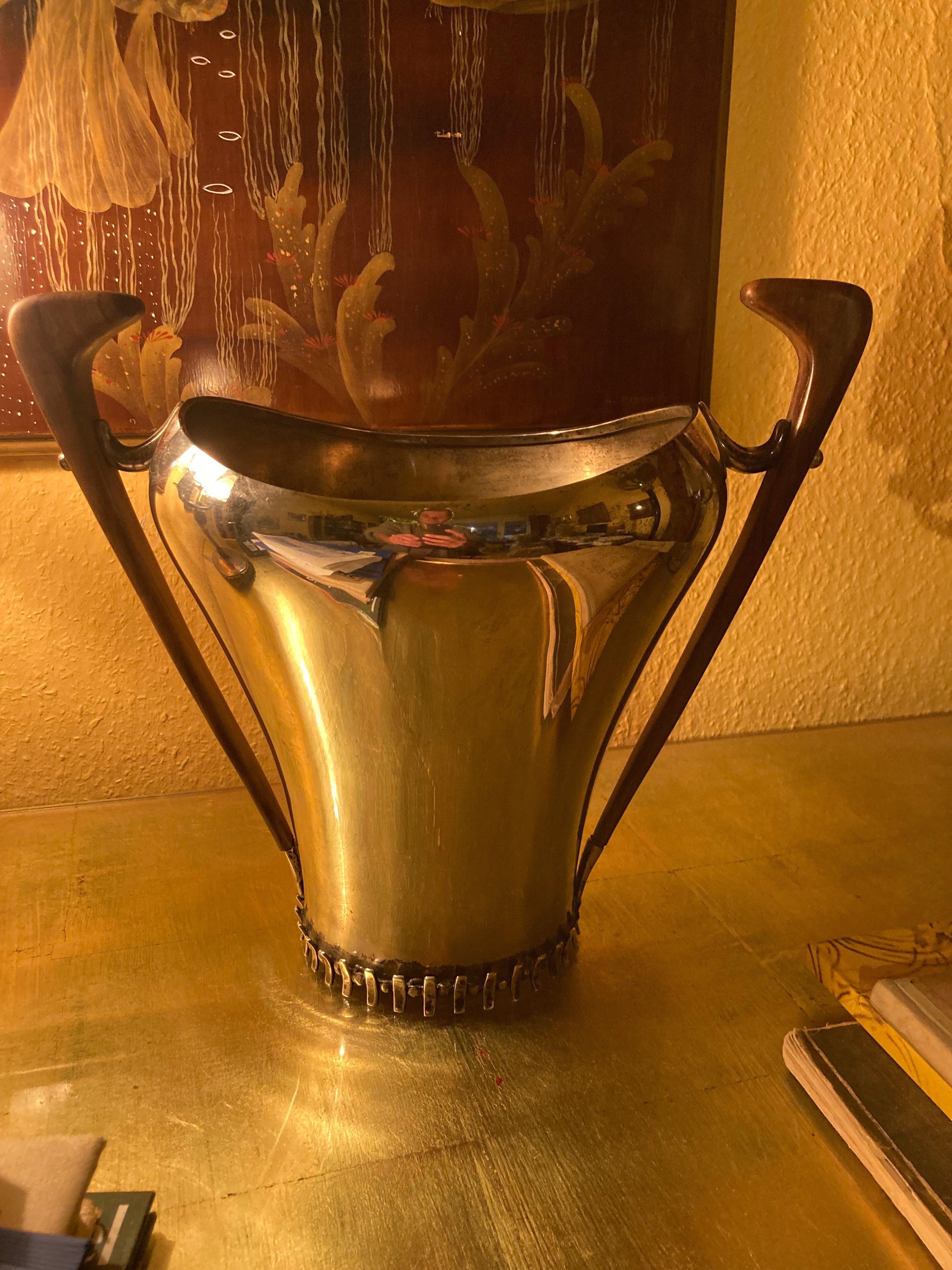 Elegante y extraordinaria nevera para vino /Champagner al estilo de Jean Despres.
800 Plata, con matasellos en la parte inferior.
Alemania, años 50.
Mangos de madera de raíz de nogal.
Cuerpo cónico.
Anillo de pie dentado circunferencial al estilo de