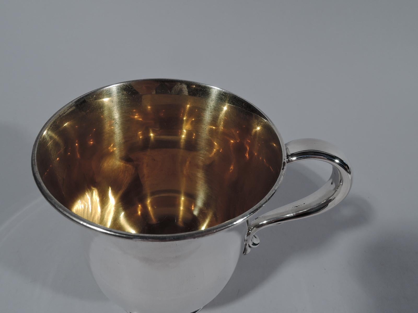 Elegant Edwardian sterling silver baby cup. Made by Tiffany & Co. in New York. Bowl has curved bottom and gently flared and molded rim. S-scroll handle and skirted foot with chased flowers and scrolls. Interior gilt washed. Fully marked including