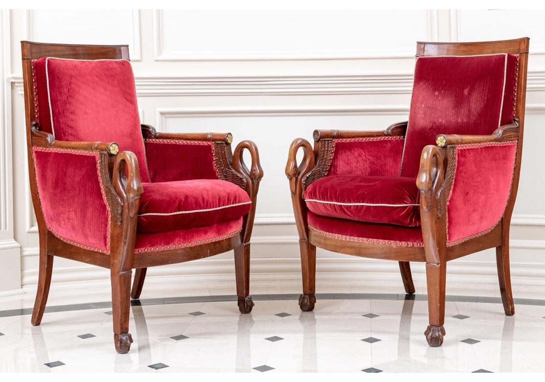 Carved fruit wood armchairs with square back and closed arms. The carved and turned arms ending in gilt rosettes and the supports with carved swans with wings. A slightly bowed seat rail raised on square front legs with stylized paw on ball feet.