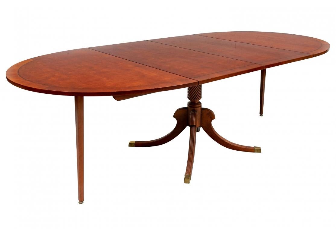 An exceptional smaller scale Oval Dining Table with fine graining and refined Line inlay. The table has a Pedestal base with Reeding and the support column has an overall swirl design. Although the table is smaller scale it can take two 20” leaves