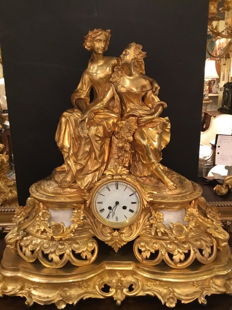 Large and impressive! Gilt bronze and white marble clock
Which consists of a lovely figural statue which sits above
A clock that has a white enamel face and Roman numerals.
The figures hold a branch of wheat and a cornucopia of
Flowers. All sit