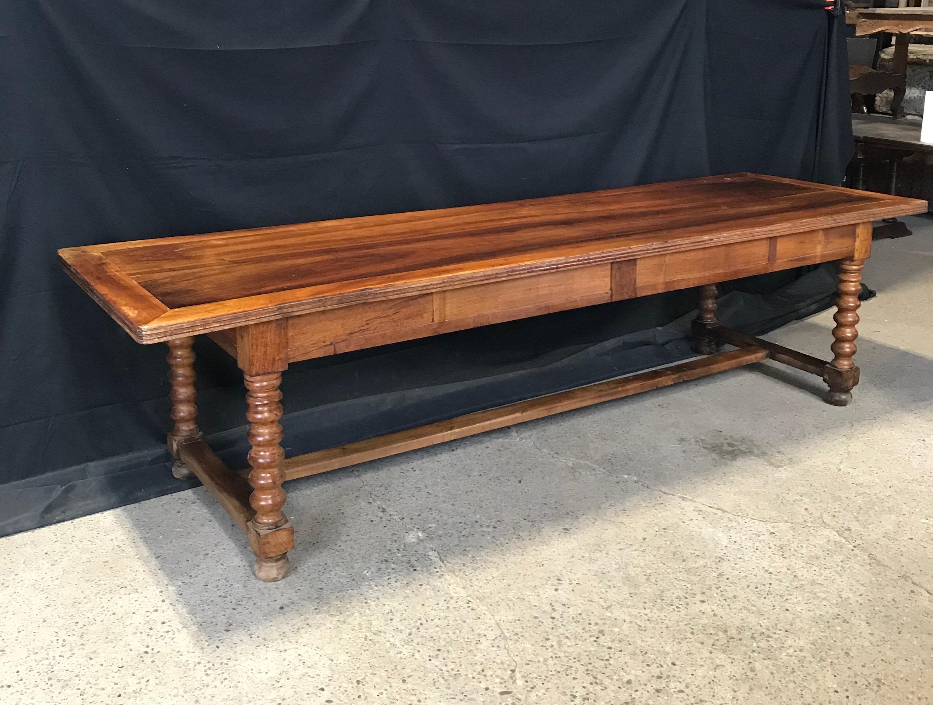 An authentic walnut expansive 9’7” long farmhouse dining table having impressive turned and carved twist legs, two drawers, and can seat up to 12. Condition: Expected surface wear and signs of use including some light surface scratching and sporadic