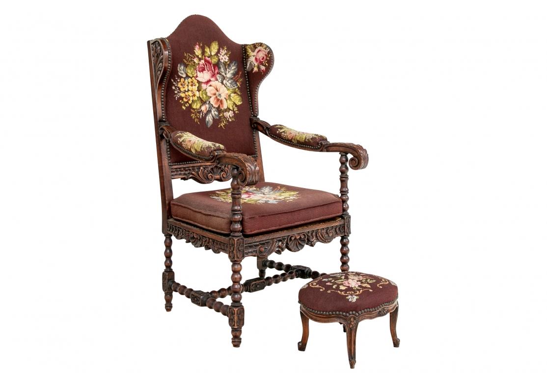 The tall shaped back with narrow carved wings and carved lower frame and seat rail. The carved scrolled leafy arm ends with turned arm supports. Raised on spool turned legs with H stretcher. Upholstered in needlepoint in brown with colored flowers