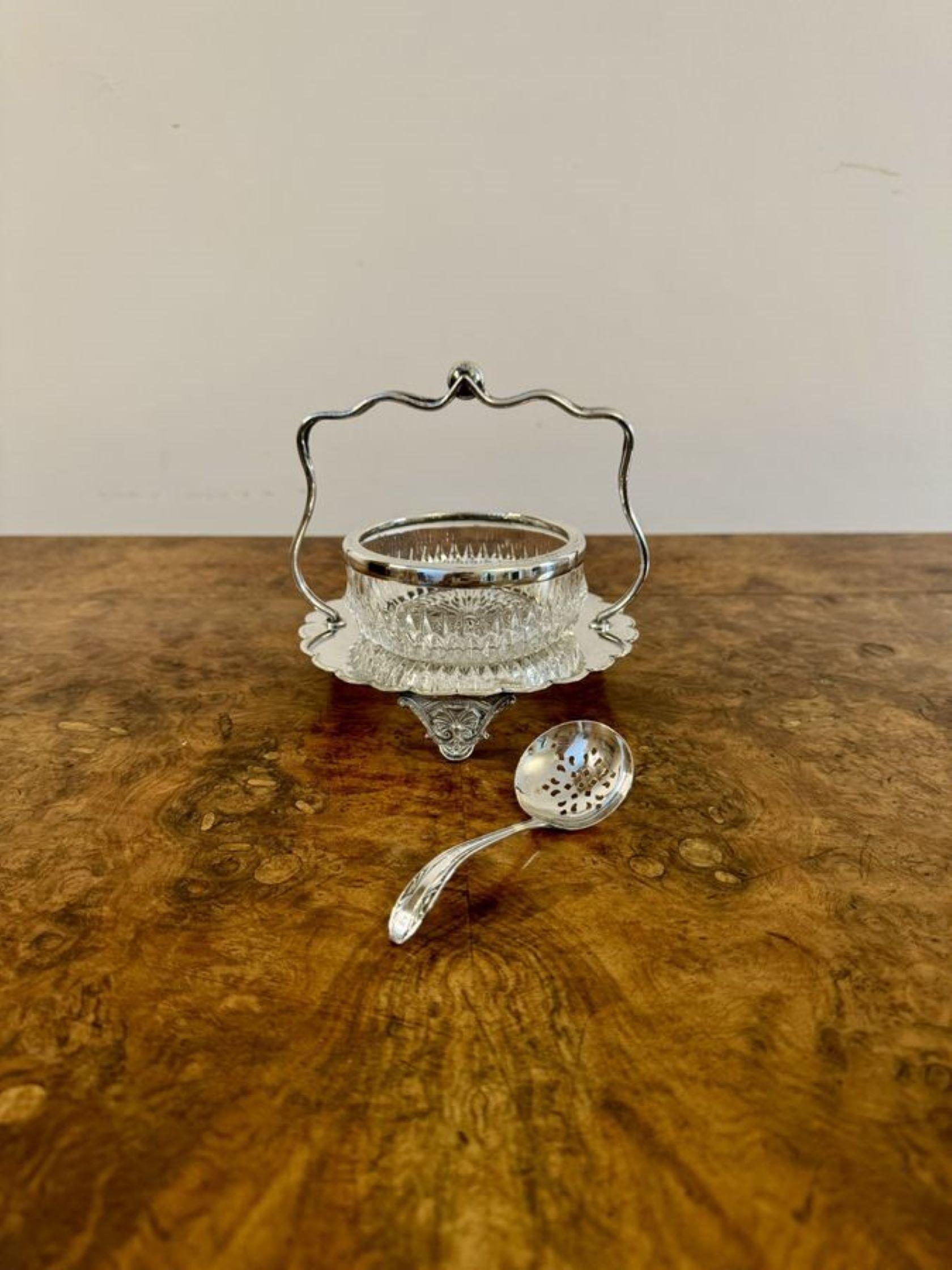 Elegant antique Edwardian silver plated jam pot and spoon, having an elegant cut glass jam pot with a silver plated rim standing on a silver plated stand with a shaped handle to the top raised on three ornate feet.

D. 1900