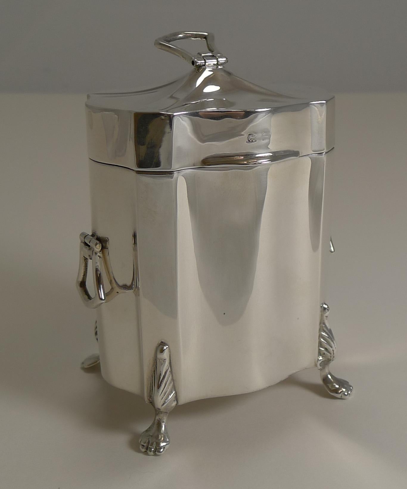 A fine example of an English sterling silver tea caddy, beautifully shaped and standing on four exquisite legs.

The top is crowned with a folding finial with two matching hinged handles to the side. The hinged lid fits perfectly and once opened