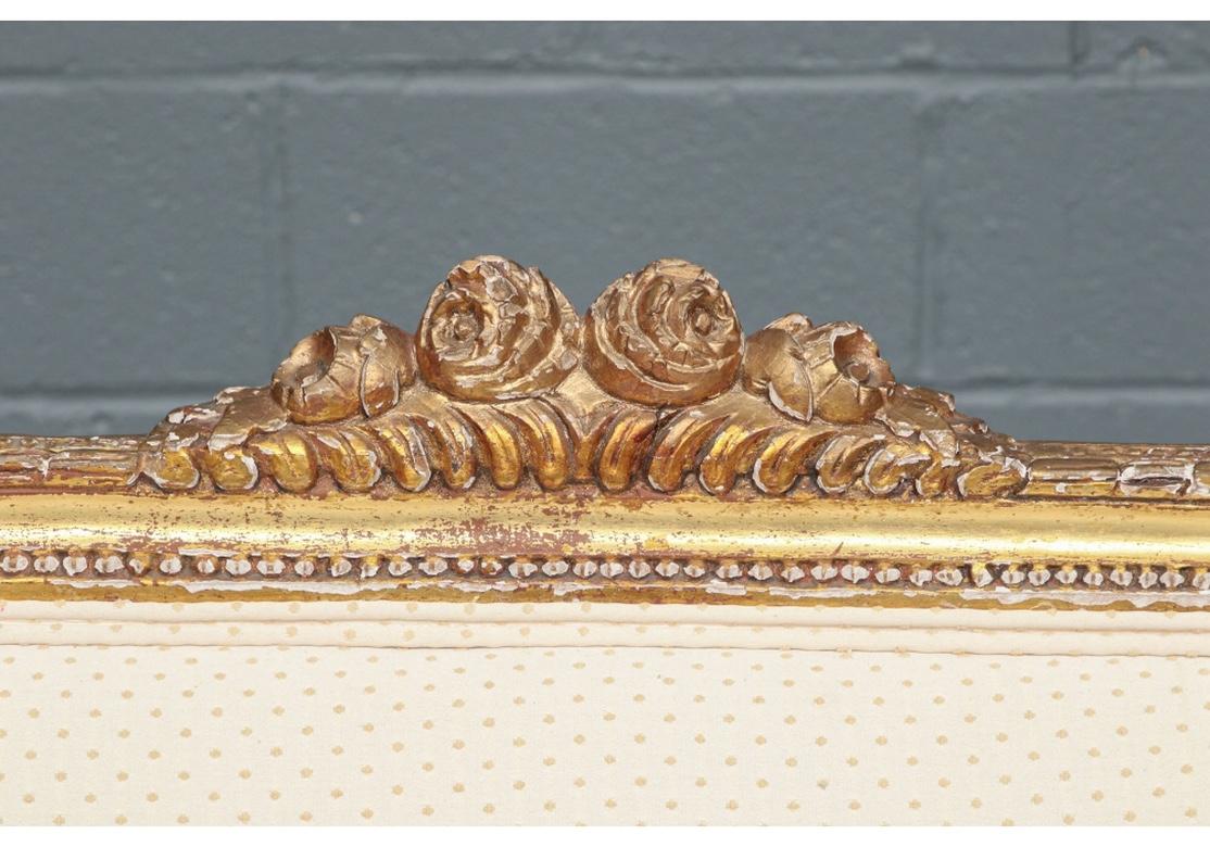 Louis XVI style, the elegant shaped frame with ribbon twist edges and and crest with roses. The upholstered arms with acanthus leaves on the ends. Raised on fluted tapering cylindrical legs. Upholstered in an ecru and golden dot fabric. 
Measures: