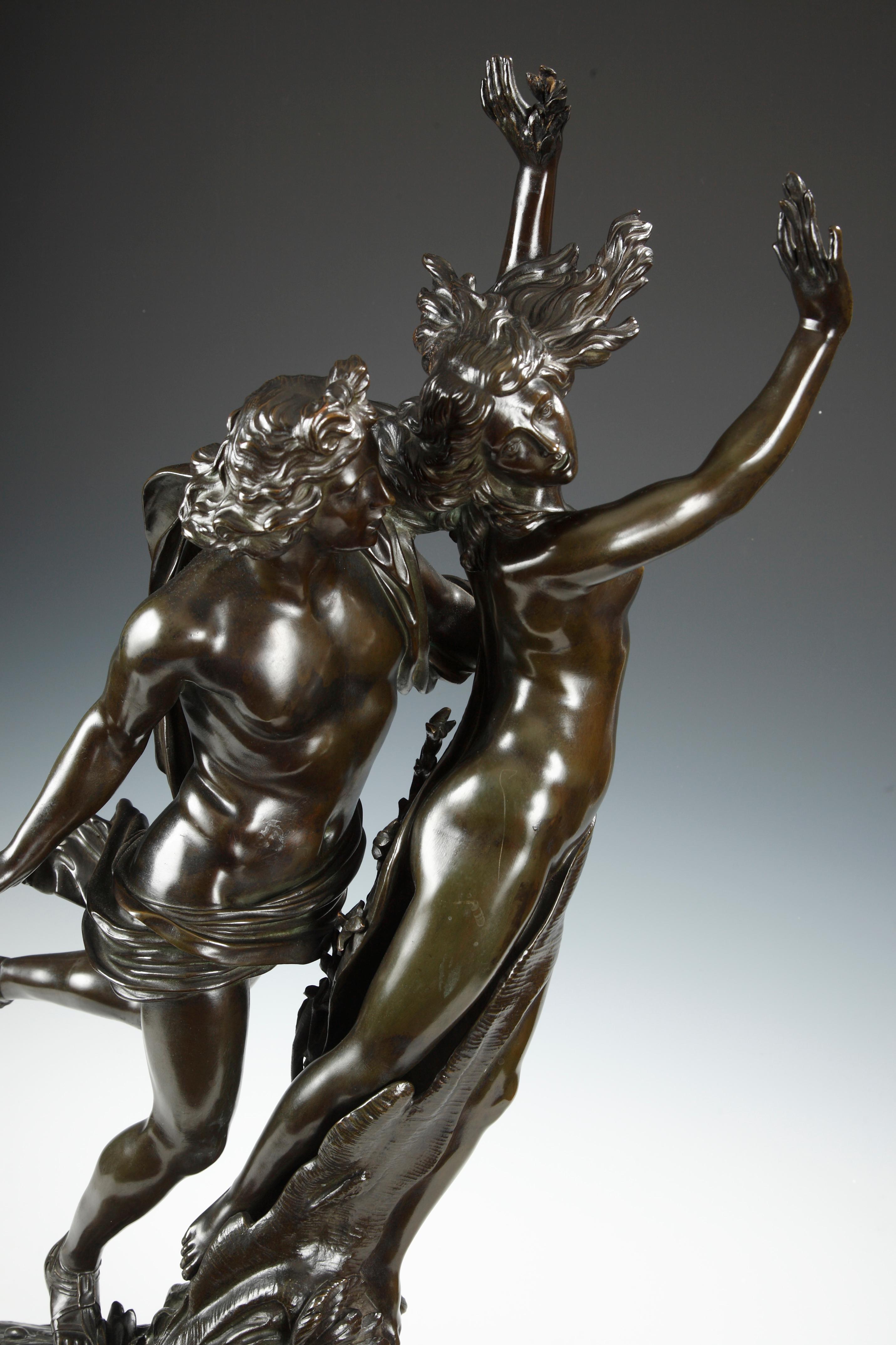 Eine Figurengruppe aus Bronze mit dunkelbrauner Patina, signiert E. Drouot, stellt Apollo dar, der Daphne verfolgt, die vor seiner Liebe fliehen wollte. Erschöpft bat sie ihren Vater, den Gott Peneus, um Hilfe. Dann verwandelte er ihre Tochter in