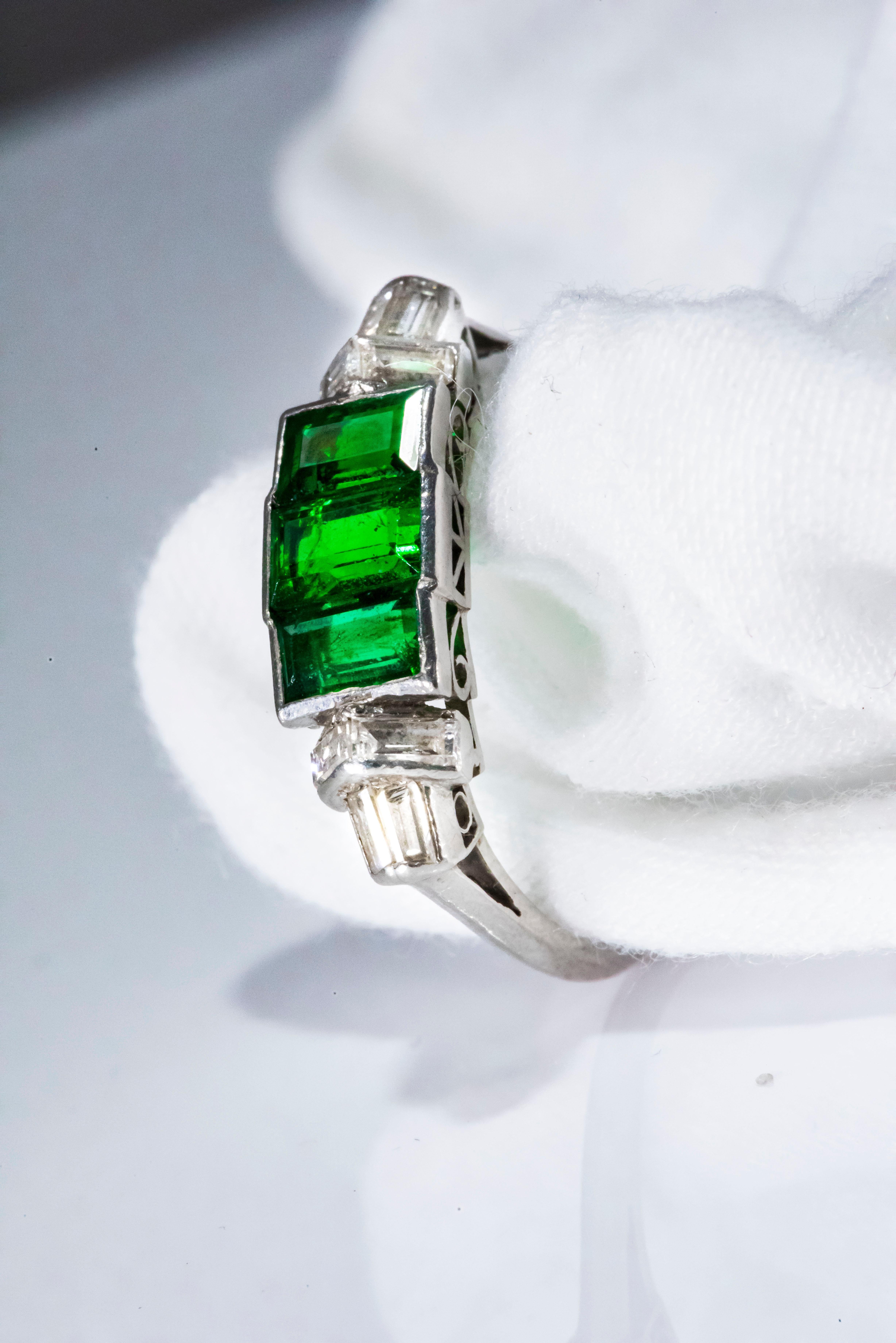 The present ring is a gorgeous example of an entirely emerald trilogy platinum ring from the 1920s. Elegant and sophisticated, this ring is entirely comprised of emerald cut stones with approximately 8 emerald cut diamonds flanking 3 larger vivid