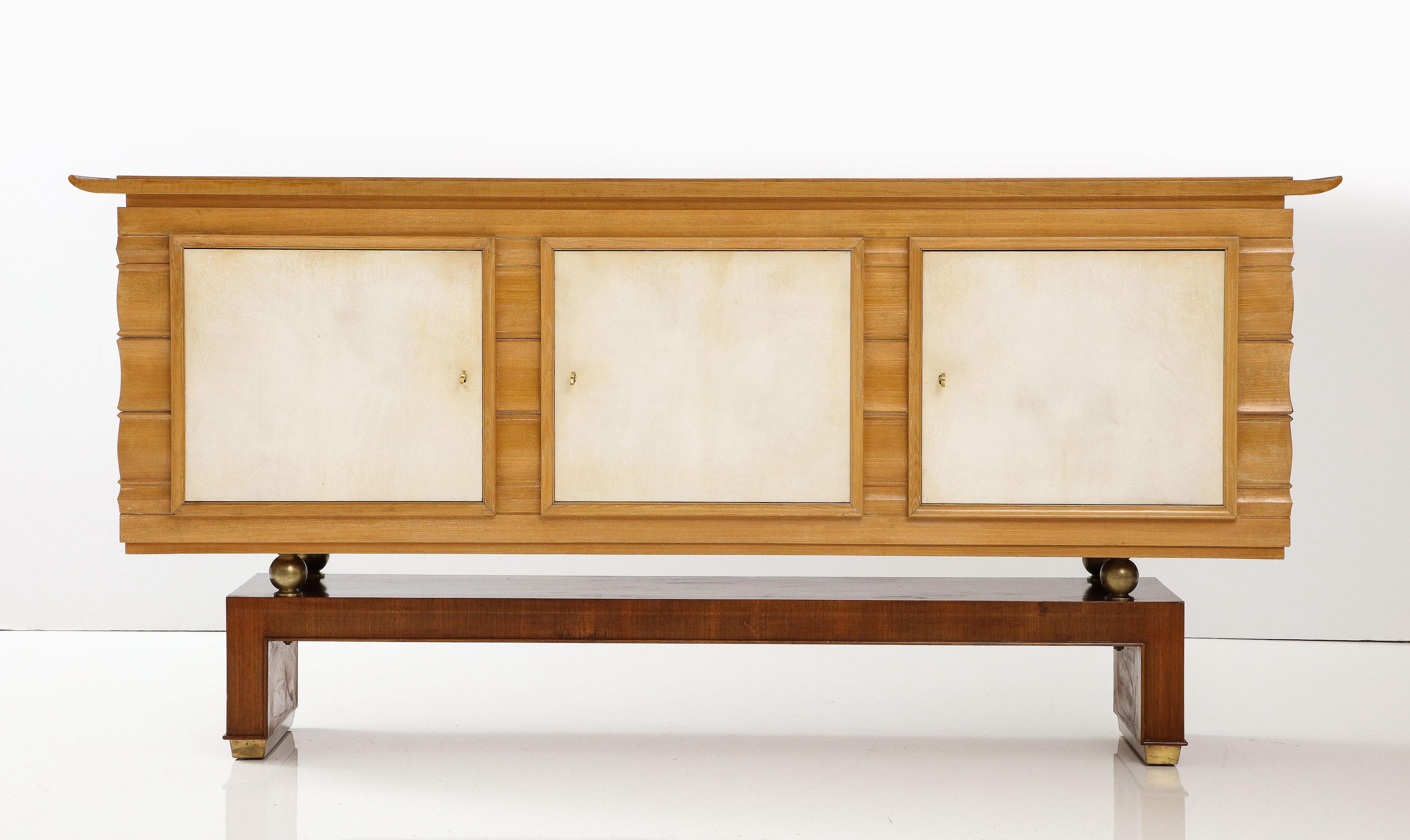 Elegant shaped oak buffet by Maxime Old with inset parchment doors resting on four polished brass ball feet over a walnut veneer platform base.   Provenance : private collection Los Angeles California.