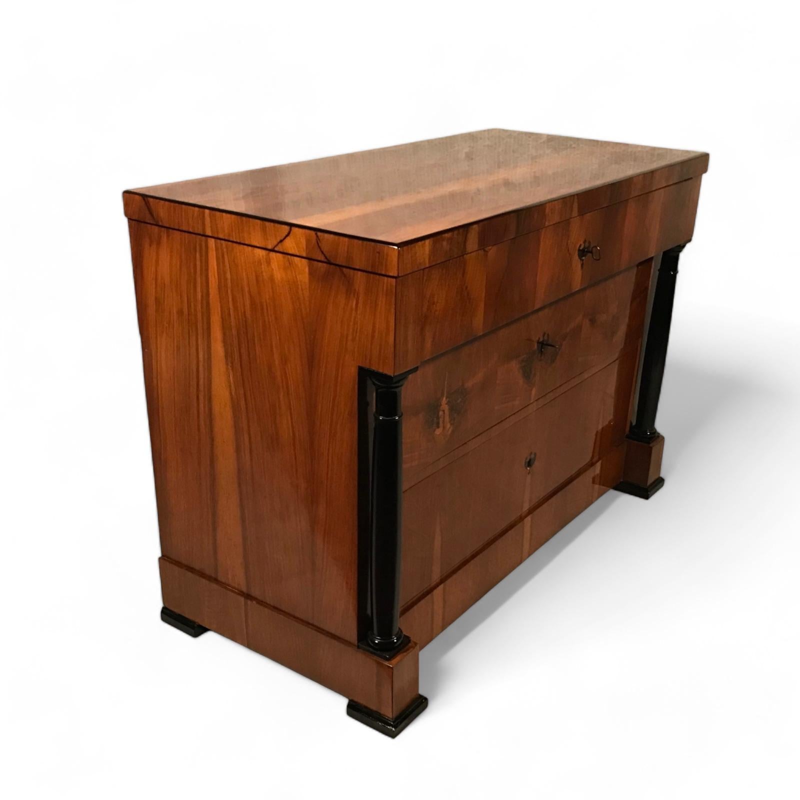 Step into history with our classic Biedermeier chest of drawers, originating from 1820 in South Germany. Crafted with exquisite walnut veneer and featuring striking ebonized columns, this piece exudes timeless elegance. With three drawers, including