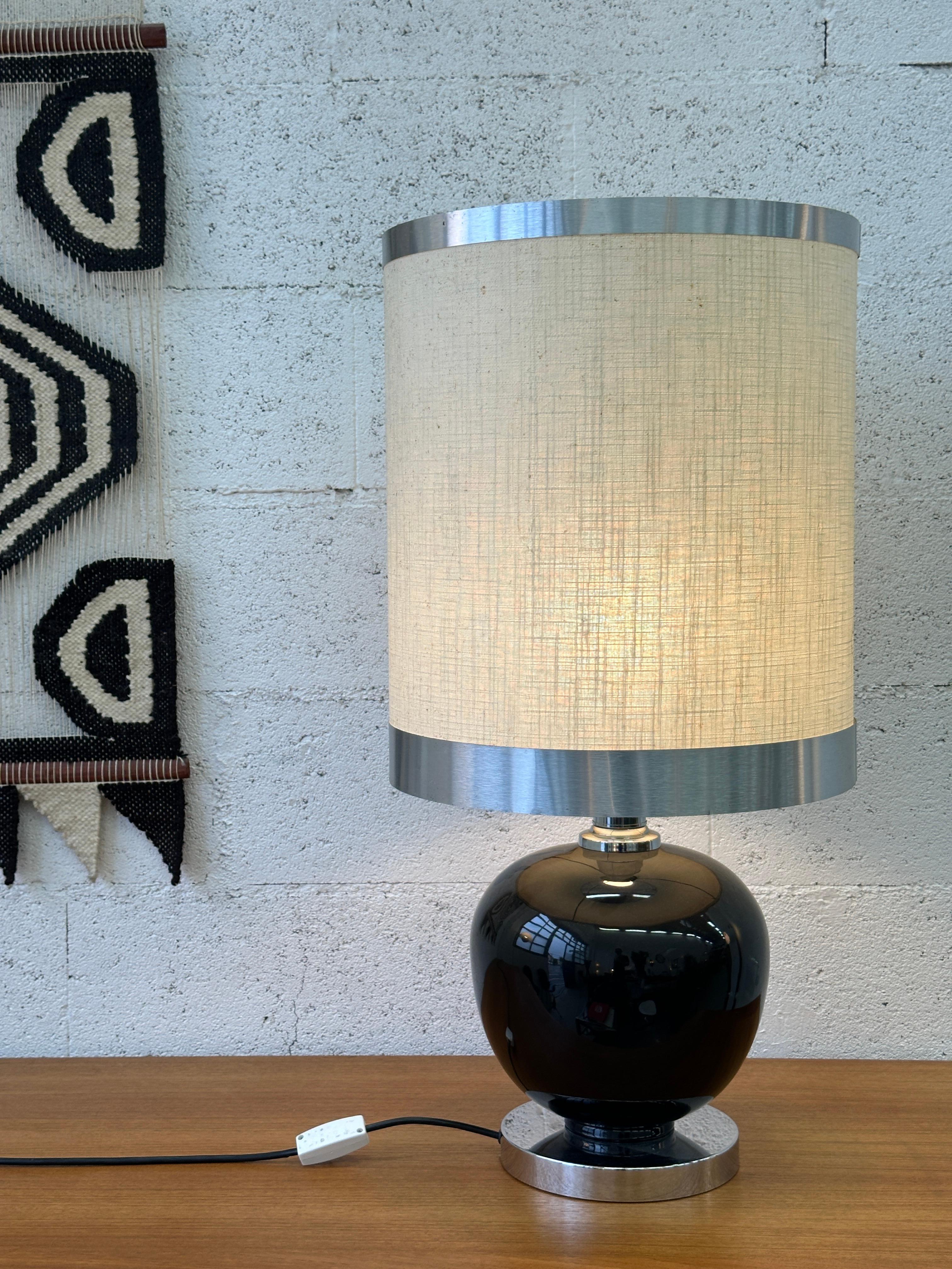 Bringen Sie einen Hauch von Raffinesse in Ihr Interieur mit dieser atemberaubenden Tischlampe. Der glänzend schwarze Keramiksockel mit verchromten Details verleiht ihm ein modernes und zugleich raffiniertes Aussehen. Der zylindrische Lampenschirm