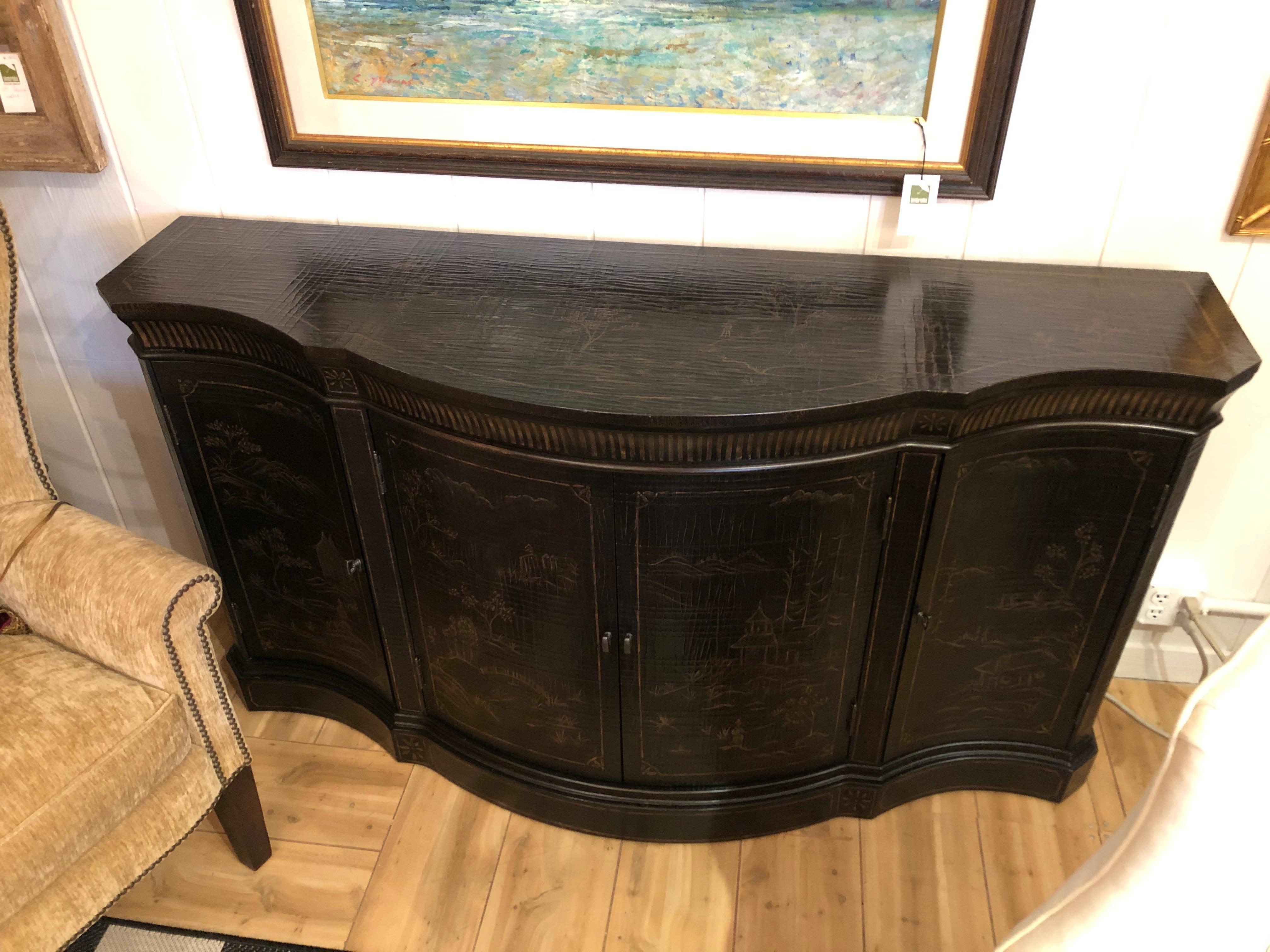 Impressive striking chinoiserie style sideboard with serpentine shape and lovely Asian motif painted decoration in gold. There is textured craquelure on the top, the central as well as side doors that open to reveal storage space.
This piece was an