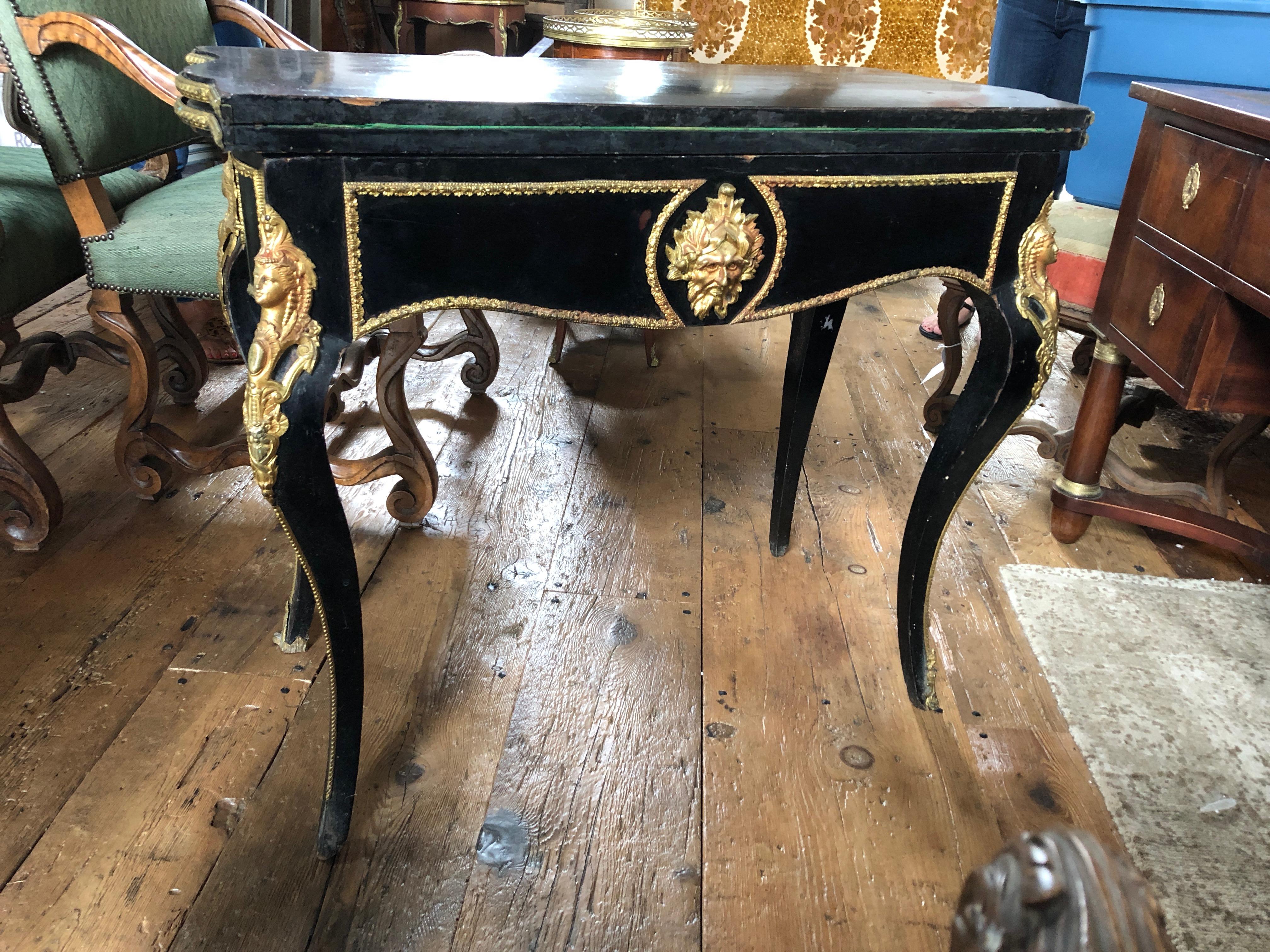 A fabulously glam French Napoleon III freestanding serpentine shaped fold over game table or console, inlaid with engraved brass trim and figures on tapering cabriole legs. The top is ebonized with good quality bronze gilt ormolu mounts and moulds.