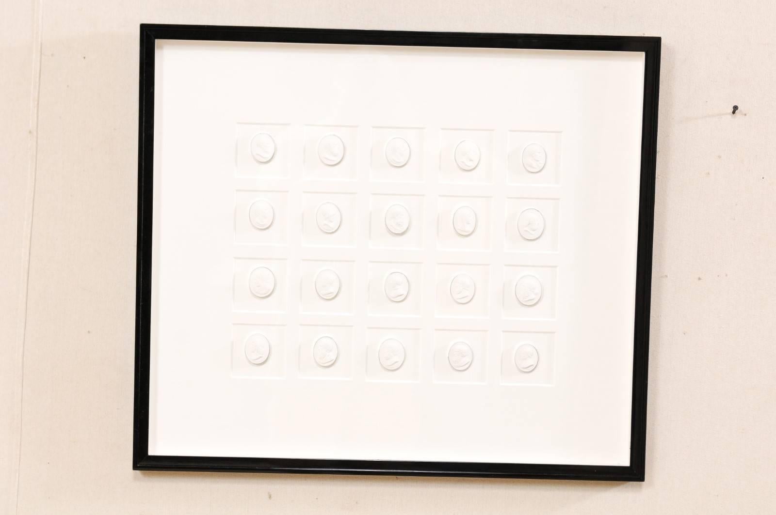 A collection of white intaglios presented within a custom black lacquer frame. This is a collection of reproduction classical profiled figure intaglios, all in a harmoniously similar size, which have been mounted and set within a custom black