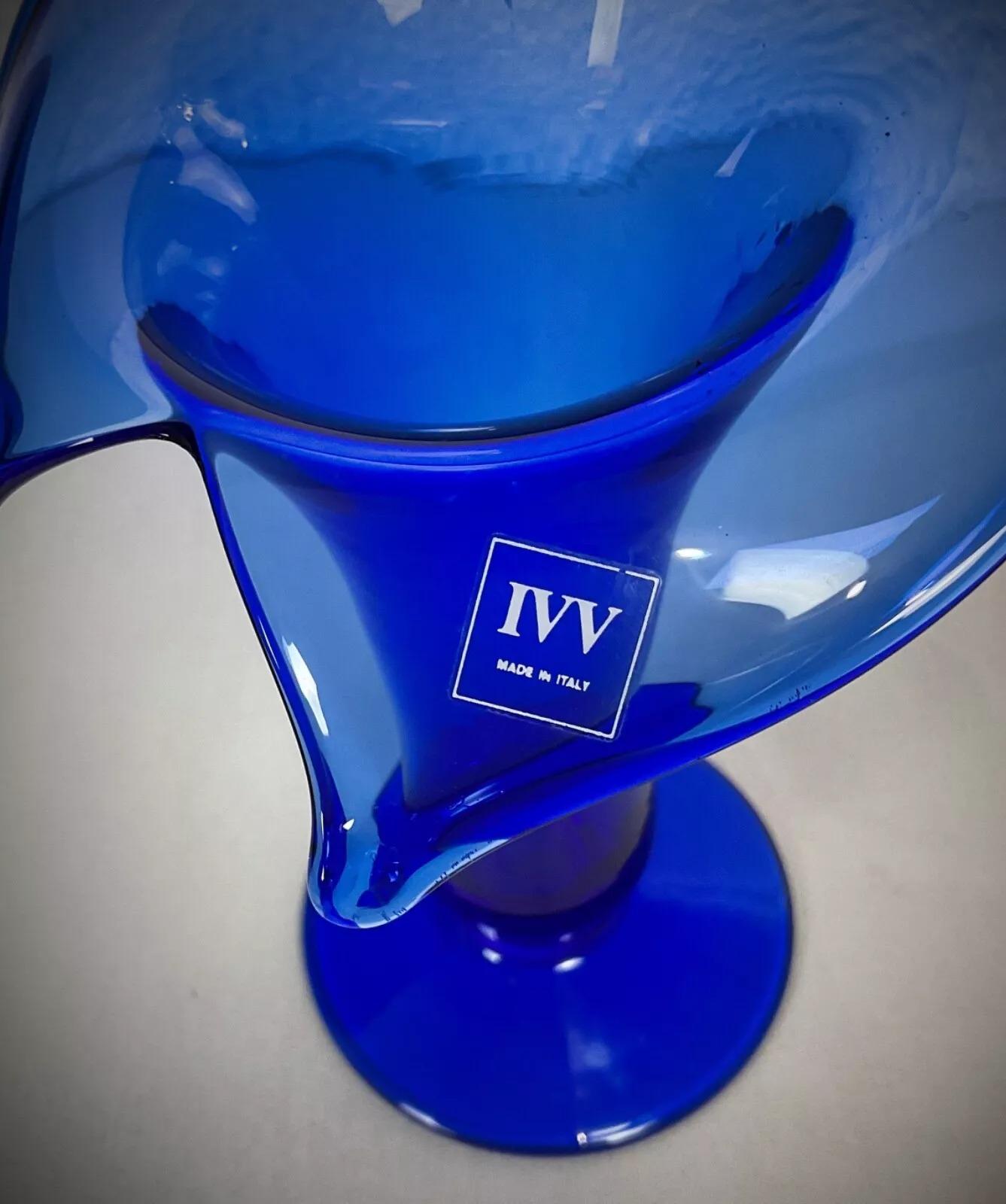 This elegant blue glass vase by IVV, made in Italy, is a beautiful addition to any home decor collection. Measuring 8.9 inches (22.5 cm) in height and 3.7 inches (9.5 cm) in diameter, this charming vase weighs 0.9 lbs (408 g) and features a sleek,