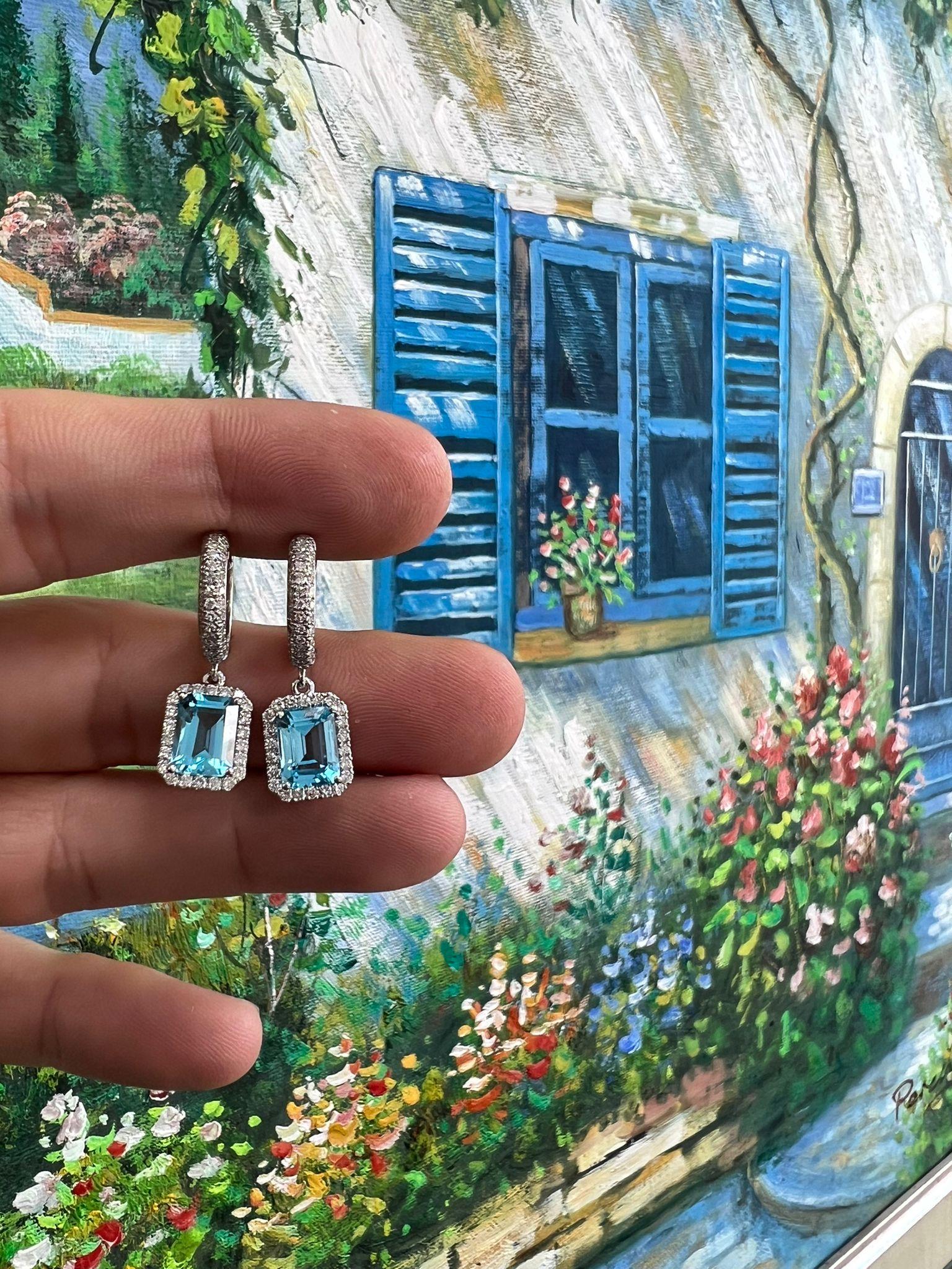 Aggiungi un tocco di raffinatezza alla tua collezione di gioielli con questi splendidi orecchini a goccia, caratterizzati da vibranti gemme di topazio blu dal taglio smeraldo che emanano un'eleganza senza tempo. Ogni topazio abbagliante è circondato