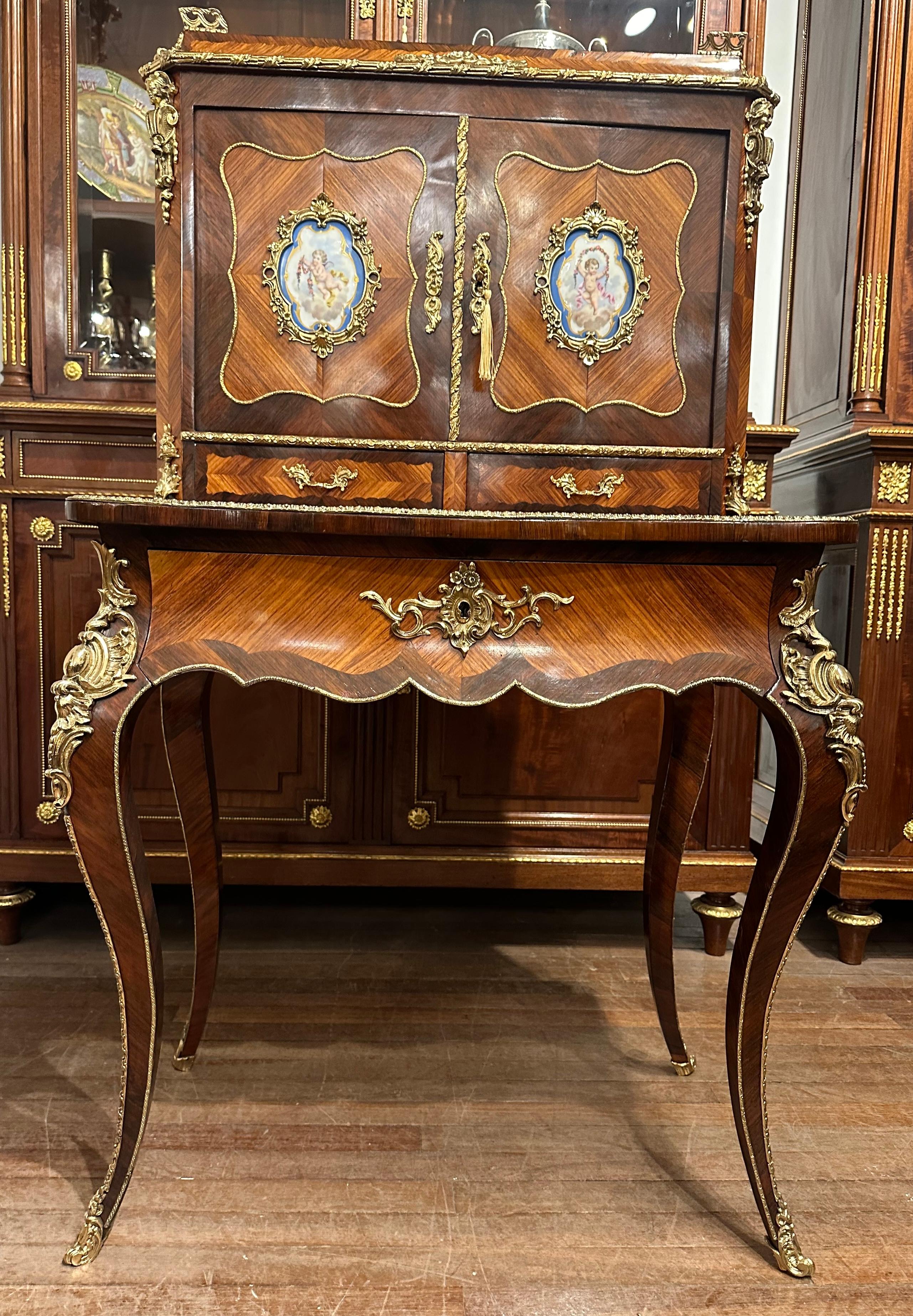 A elegant French bonheur de jour ladies writing desk in kingswood and rosewood, with bronze gilt ormolu mounts to the legs and hand painted Sevres plaques. There is a sliding red leather writing leaf, complete with key.
Bonheur de Jours were