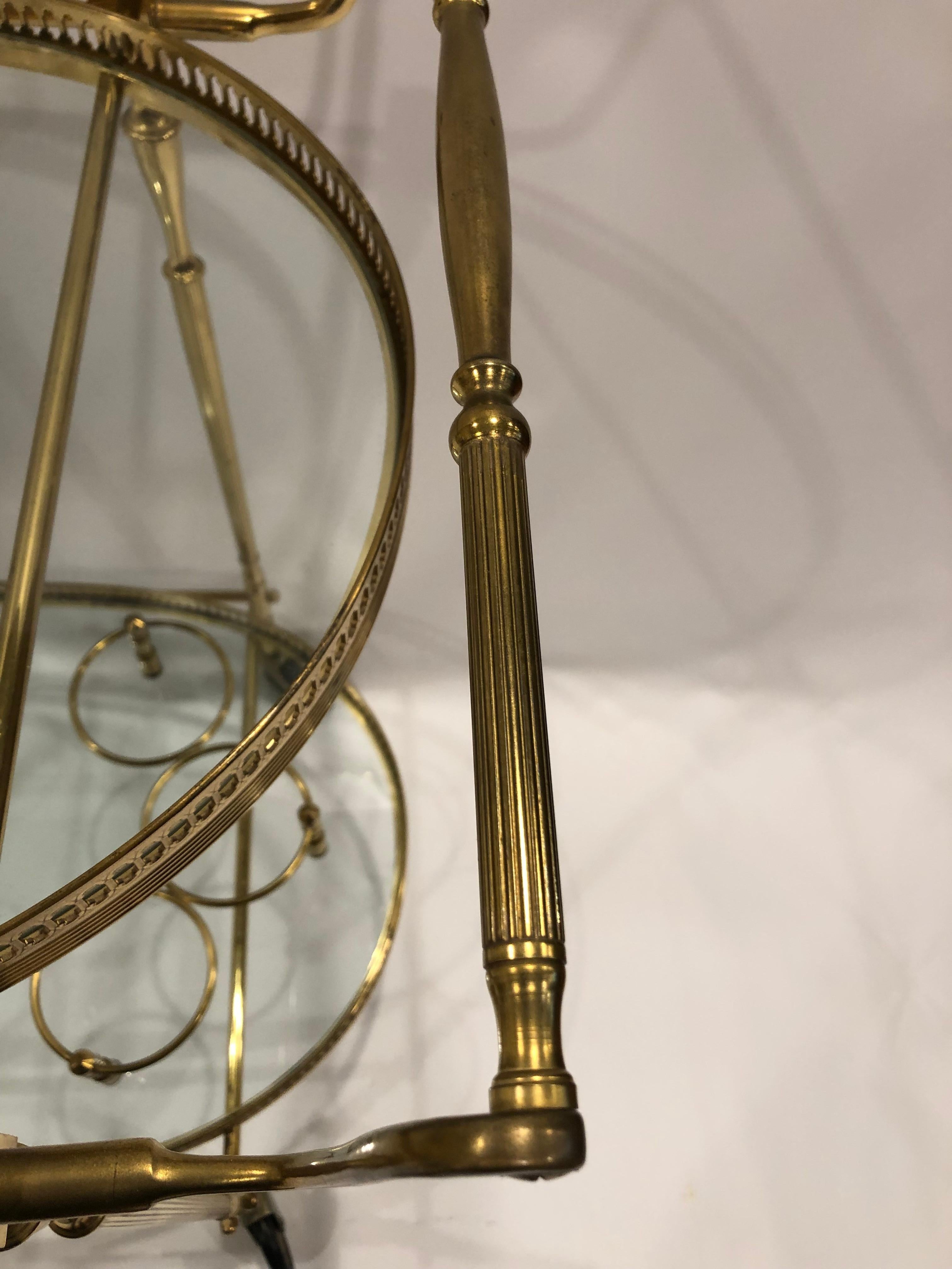 Classically elegant vintage brass bar cart having two oval tiers with pierced galleries, bottle holder, and smoothly functioning pretty wheels.