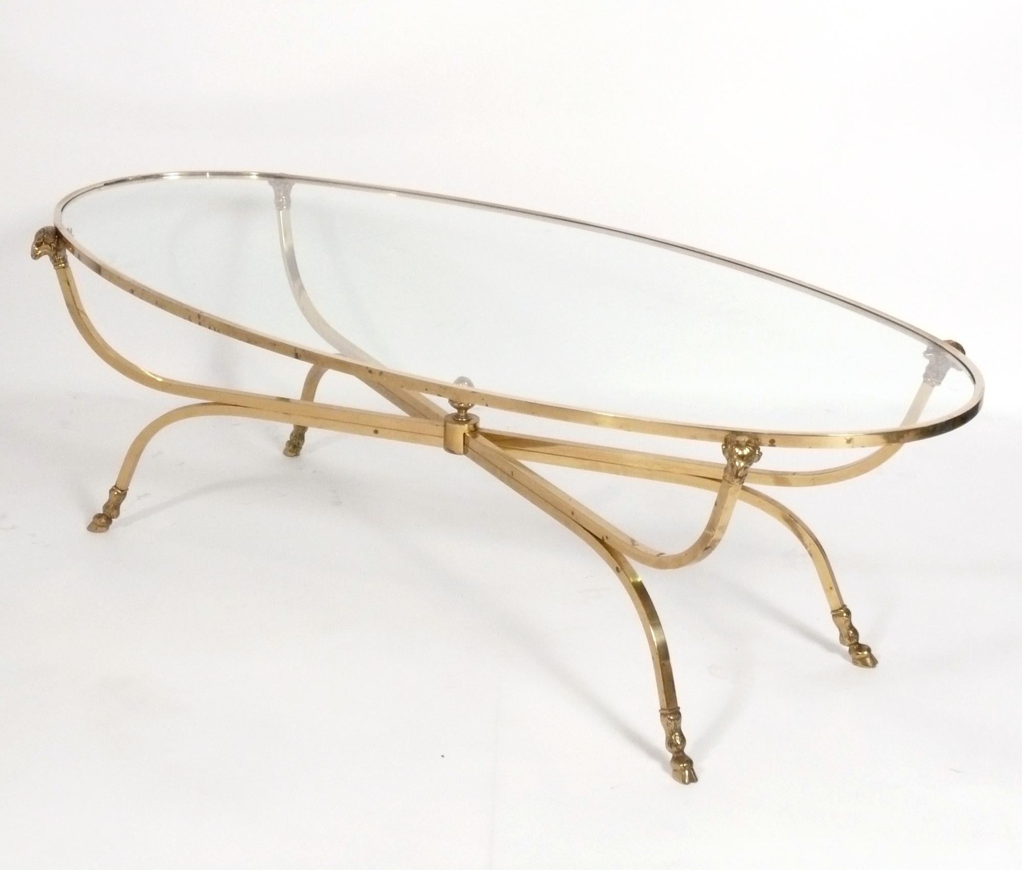 Elegant brass rams head coffee table in the manner of Maison Jansen, unsigned, French, circa 1950s. This coffee table is a very high quality construction, with crisp casting to the ram’s heads at the top, as well as their hoofed feet at the bottom.