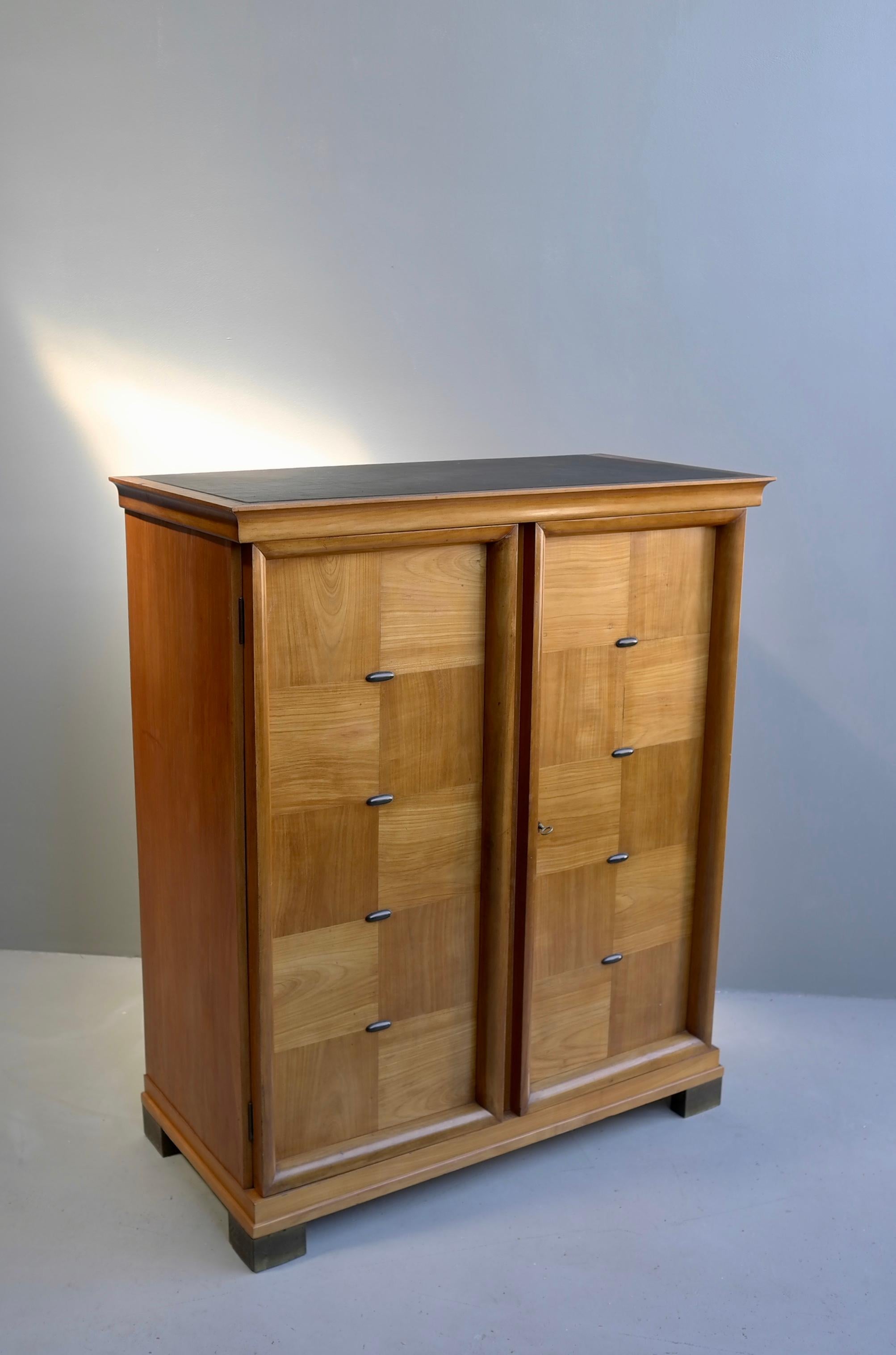 Elegant cabinet with black leather top, in style of Jacques Adnet, France, 1940s.
With fine brass details at the doors and brass feet with patina.
   