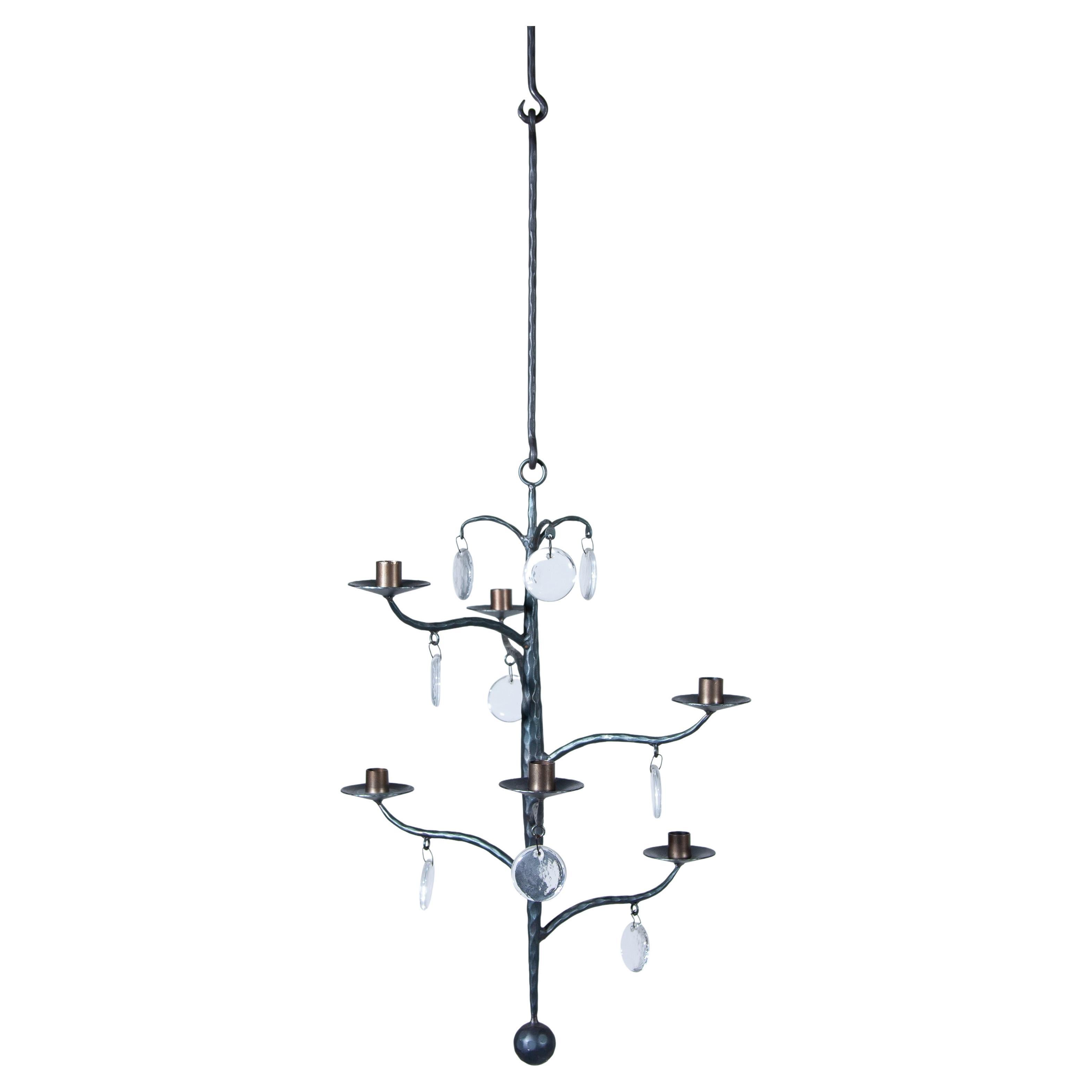 An elegant chandelier hand-forged chandelier with 6 arms for 6 candles and glass, designed by Swedish artist Erik Höglund for Boda. Light-reflecting glass medallions hang in each arm. In the upper part of the chandelier hang 3 more medallions made