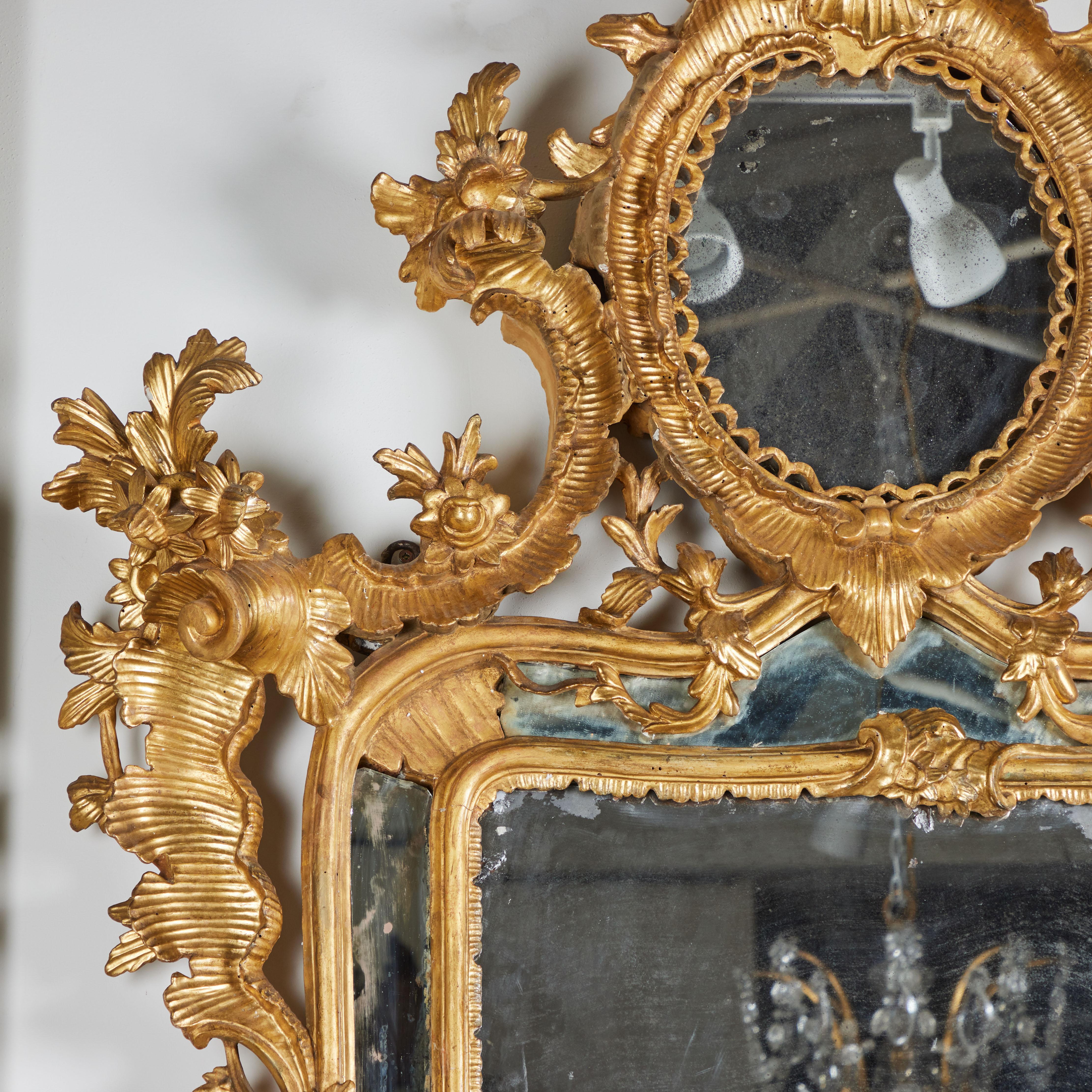A hand carved, gessoed and gilded framed mirror with floral and vine designs.  Original glass with age-appropriate spotting and loss of silvering to plates.  
