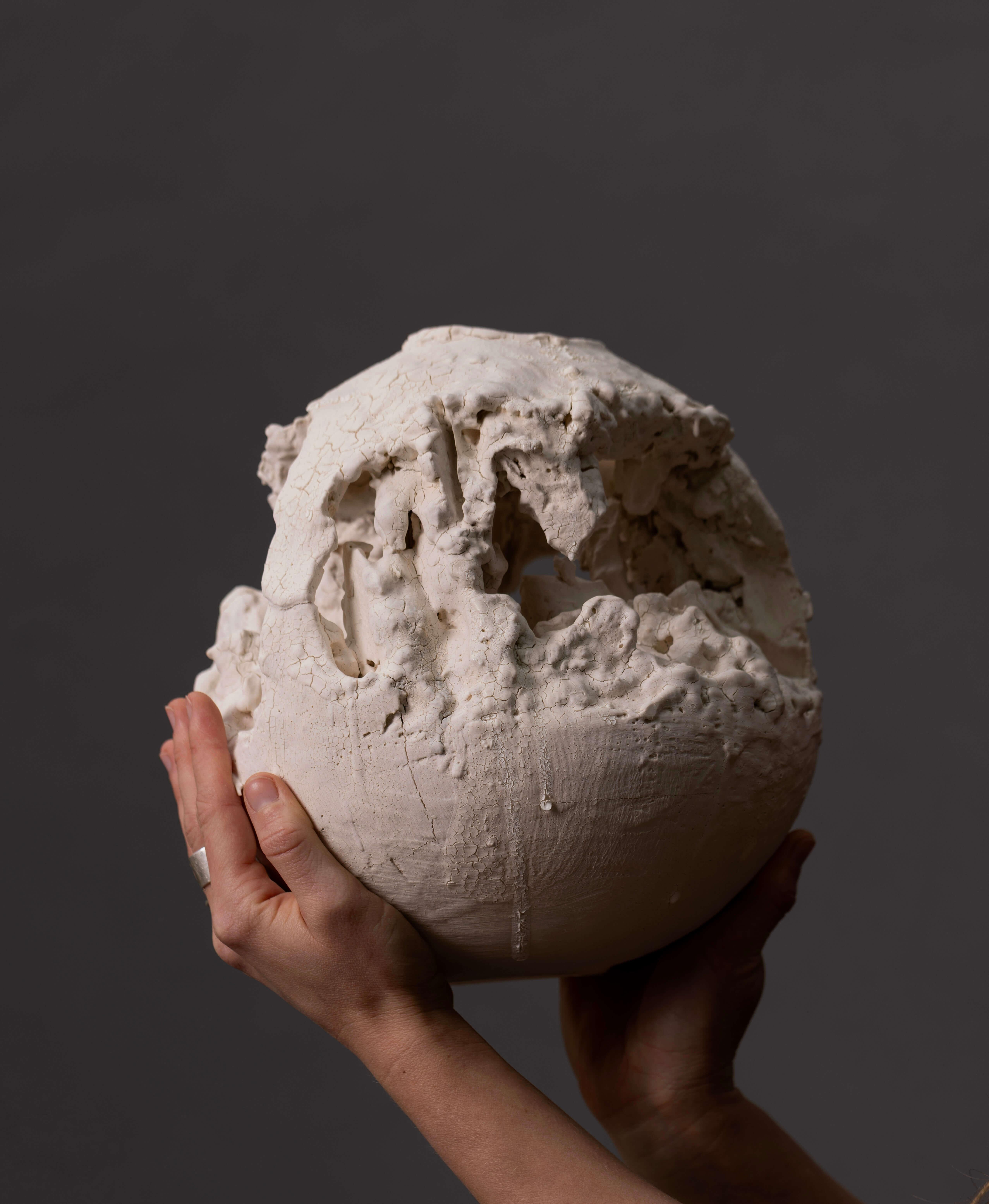 This handmade ceramic vase has a light beige color and a rounded shape with a distinctive, textured surface. The surface is heavily textured with cracks, crevices, and an uneven finish that gives it a raw, natural appearance. Unlike traditional