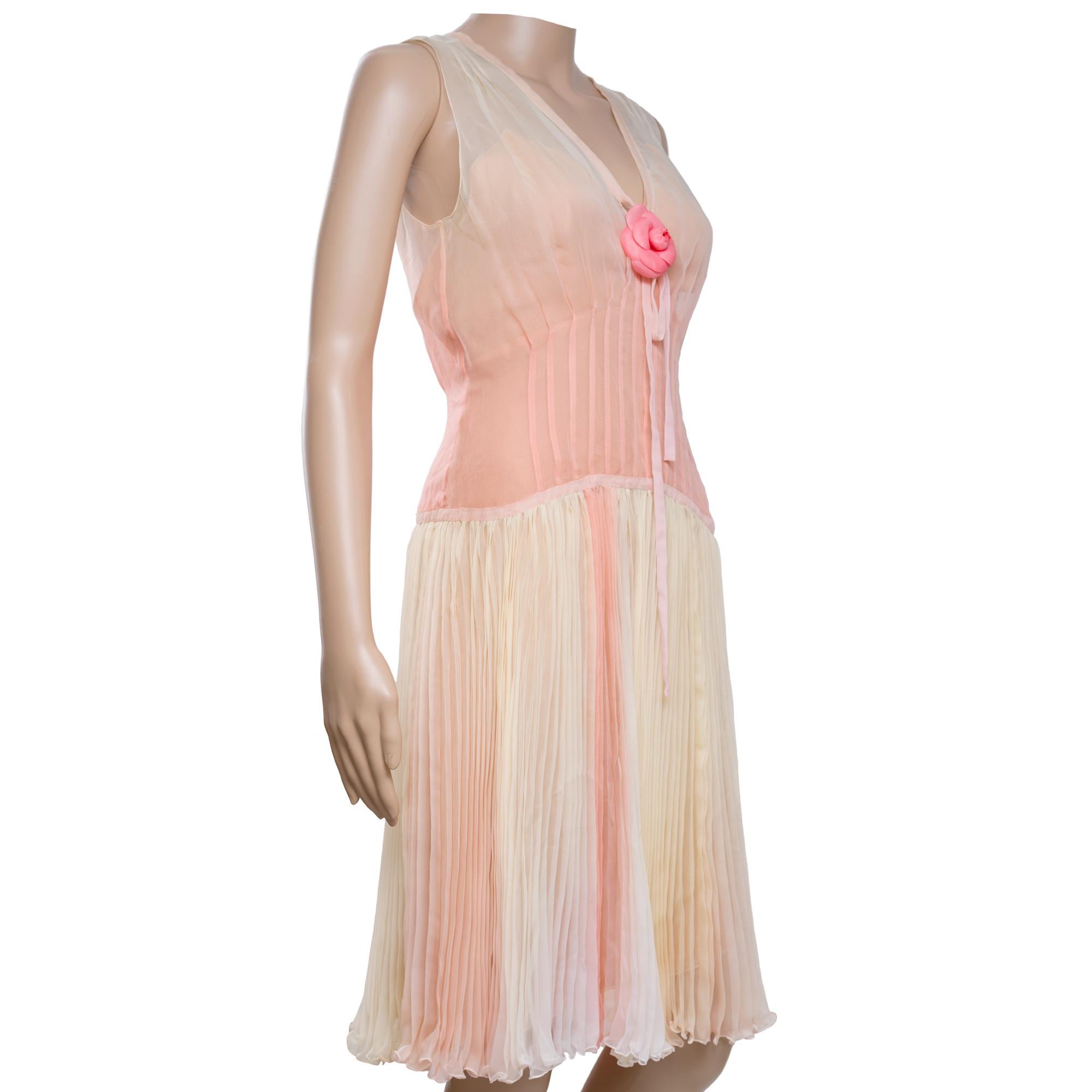 Elegant​ ​Chanel​ ​100%​ ​Silk​ ​Pleated​ ​Dress​ ​with​ ​Rose​ ​Detail
This​ ​Chanel​ ​silk​ ​dress​ ​exudes​ ​elegance​ ​with​ ​its​ ​peach-toned​ ​sheer​ ​bodice,​ ​V-neckline,​ ​and​ ​a​ ​central​ ​silk​ ​rose​ ​embellishment​ ​with​ ​ribbon​
