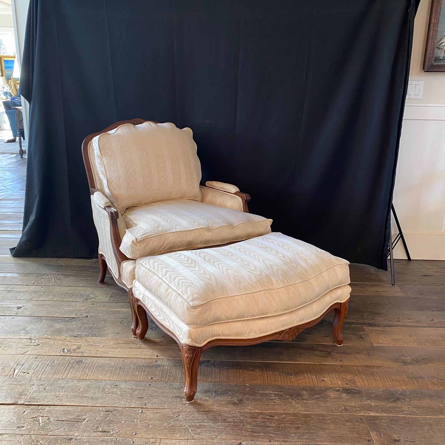 Inviting luxurious French Louis XV style carved walnut and upholstered club chair with coordinating ottoman having fluted legs and rosettes. This set retains its original neutral ivory fabric; still in good shape. The scalloped top of back cushion