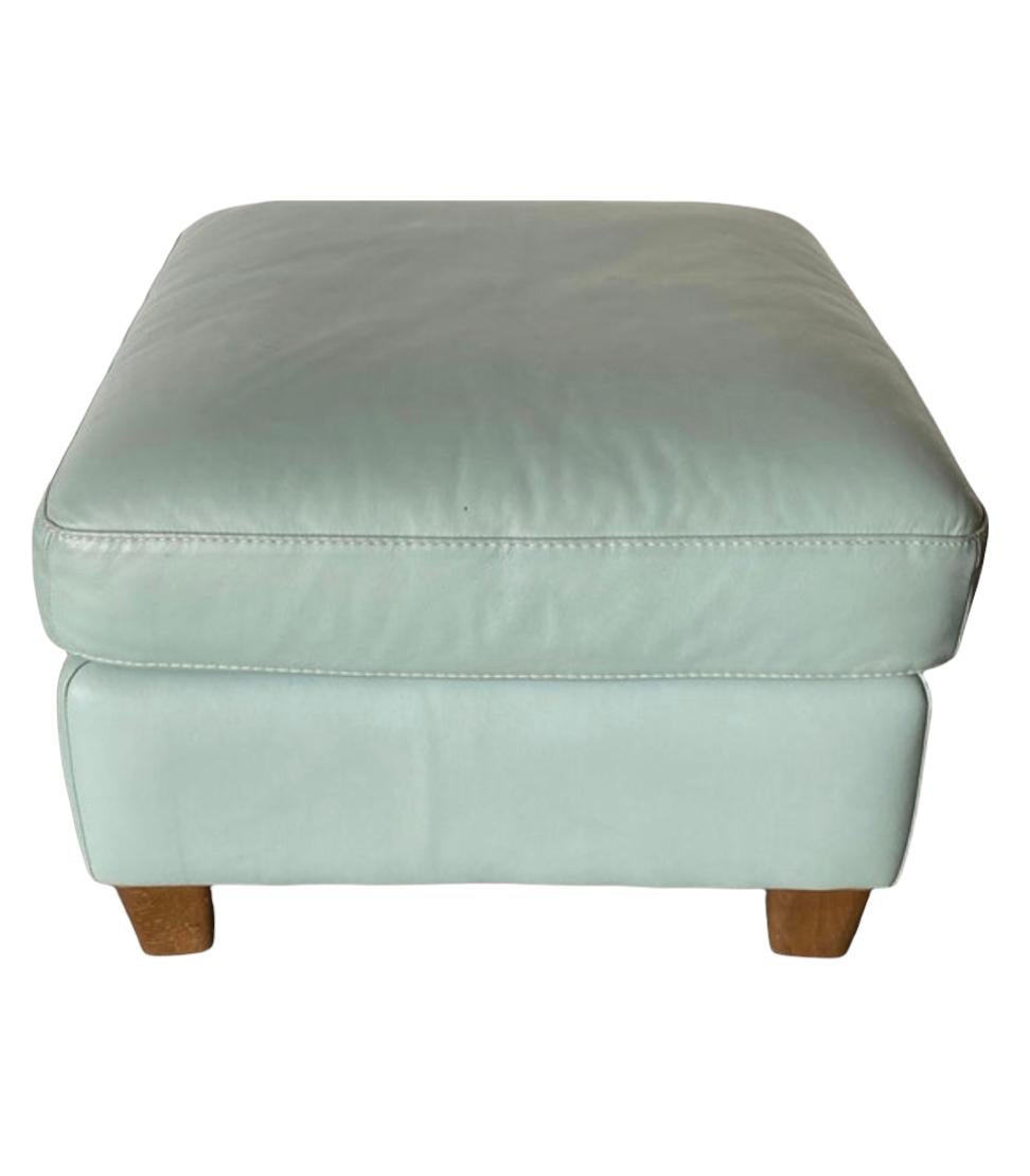 Elegant ottoman executed in soft turquoise leather. Free of tears or dryness. Sits atop walnut legs. Solid and sturdy, can easily support the weight of a person and be used as a seat or ottoman. 