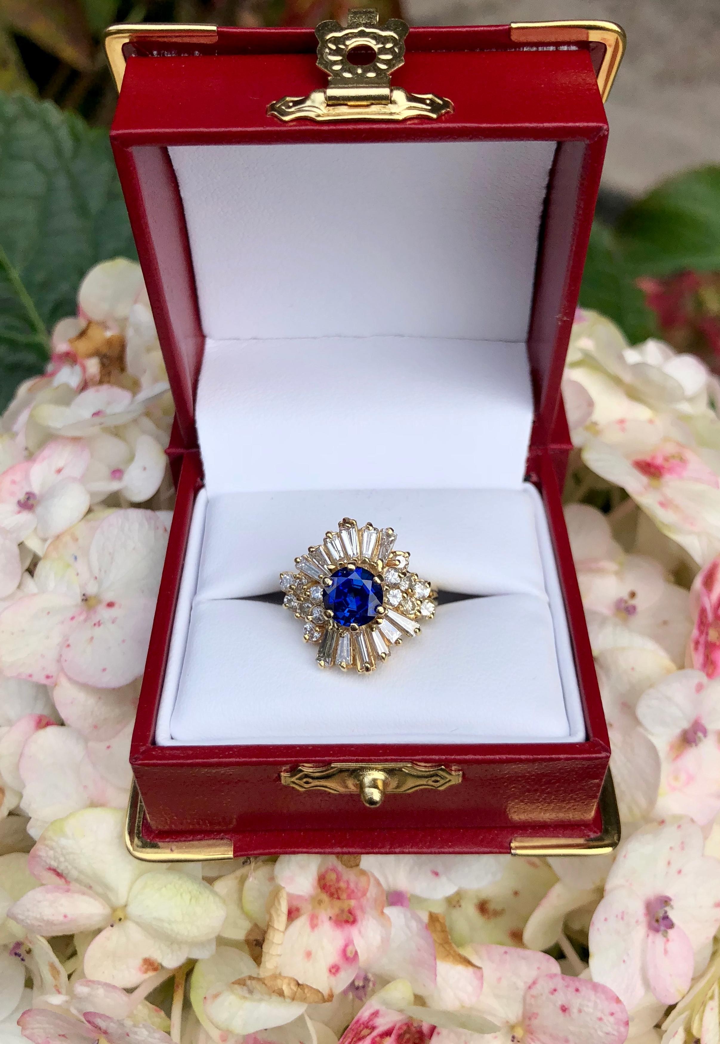 Classic ballerina style 14 karat yellow gold estate ring features a vivid, cornflower blue round blue sapphire, prong set with 6 prongs, and surrounded by 2 carats of long, prong set tapered baguettes and prong set round brilliant diamonds. Sapphire